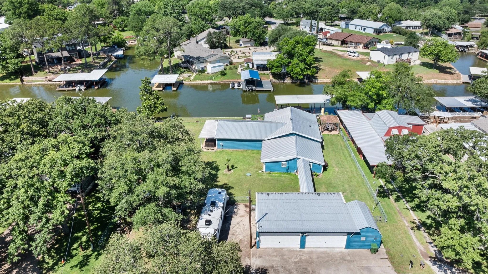 Waterfront property featuring a main residence with a blue exterior and metal roof, an adjacent two-car garage with a matching exterior, and a private boat dock