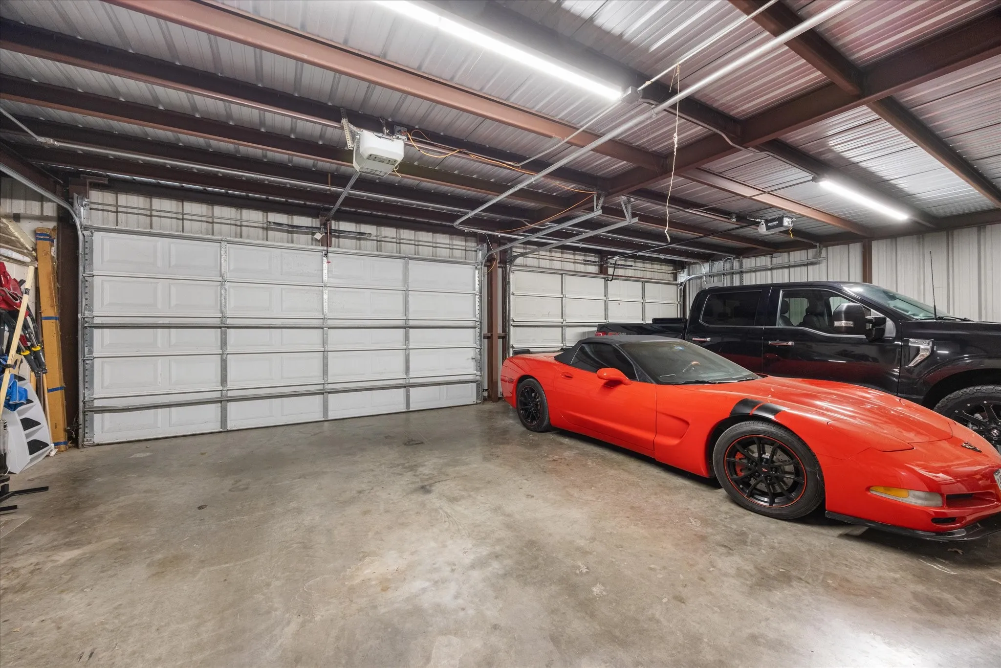 Spacious metal-frame structure featuring two paneled garage doors, a concrete floor, and ample overhead lighting