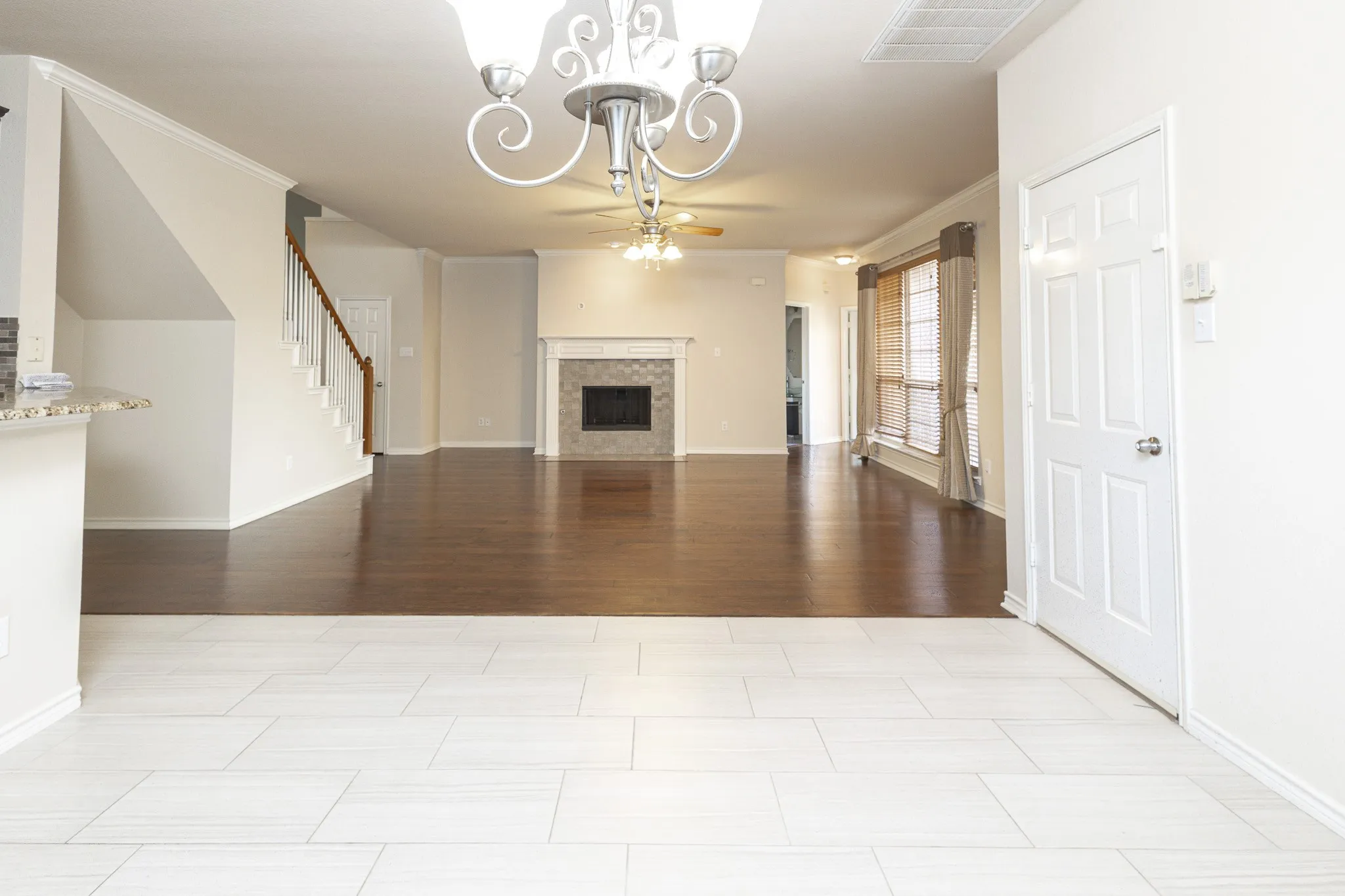 Unfurnished living room featuring crown molding, a tiled fireplace, light tile floors, and ceiling fan with notable chandelier