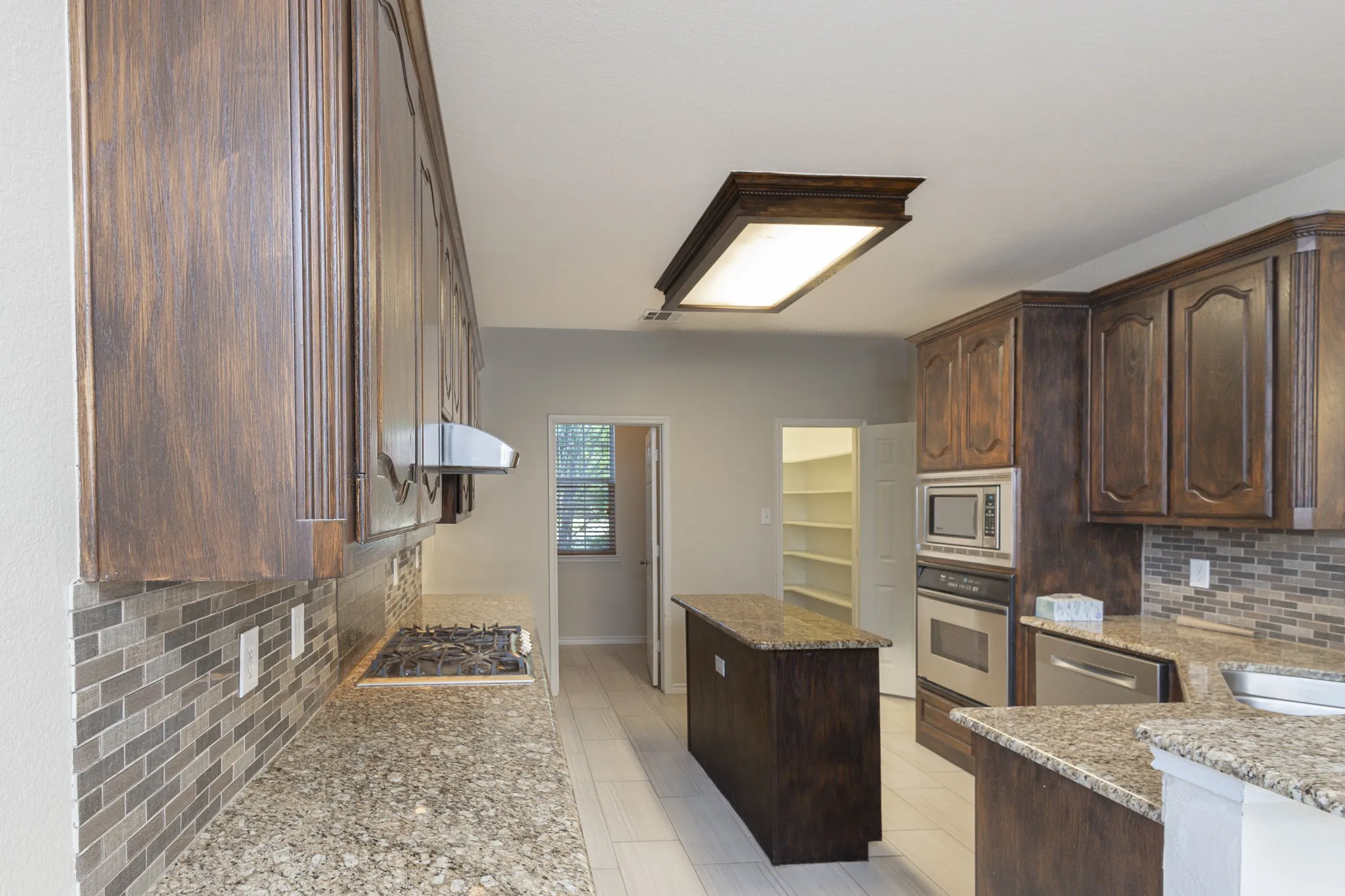 Kitchen featuring stainless steel appliances, light stone counters, dark brown cabinetry, tasteful backsplash, and light tile flooring