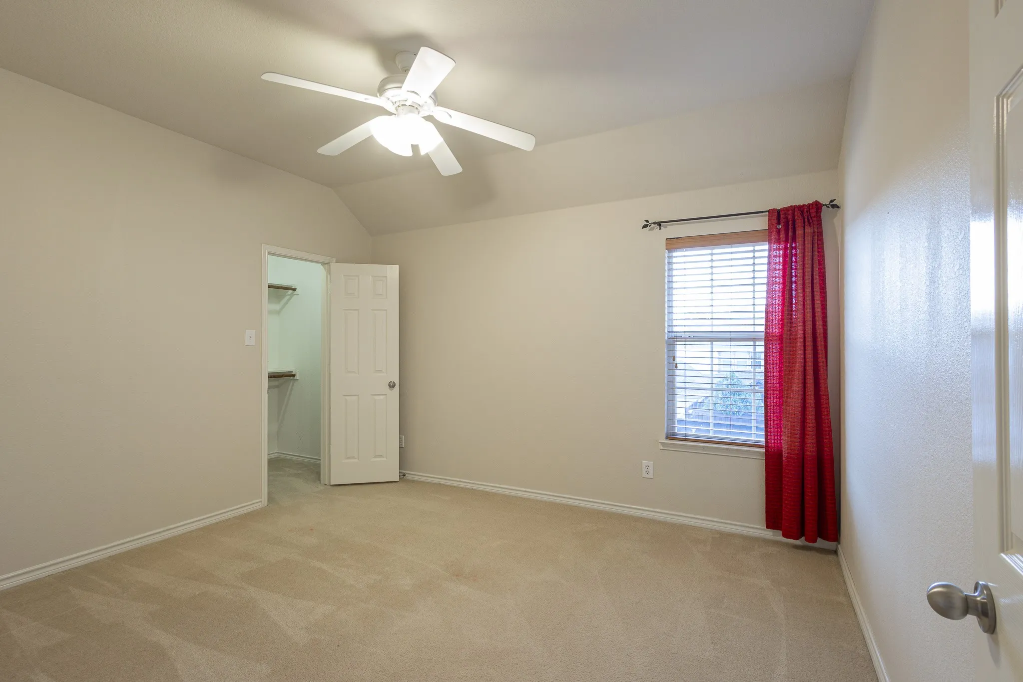 Carpeted empty room featuring ceiling fan and lofted ceiling