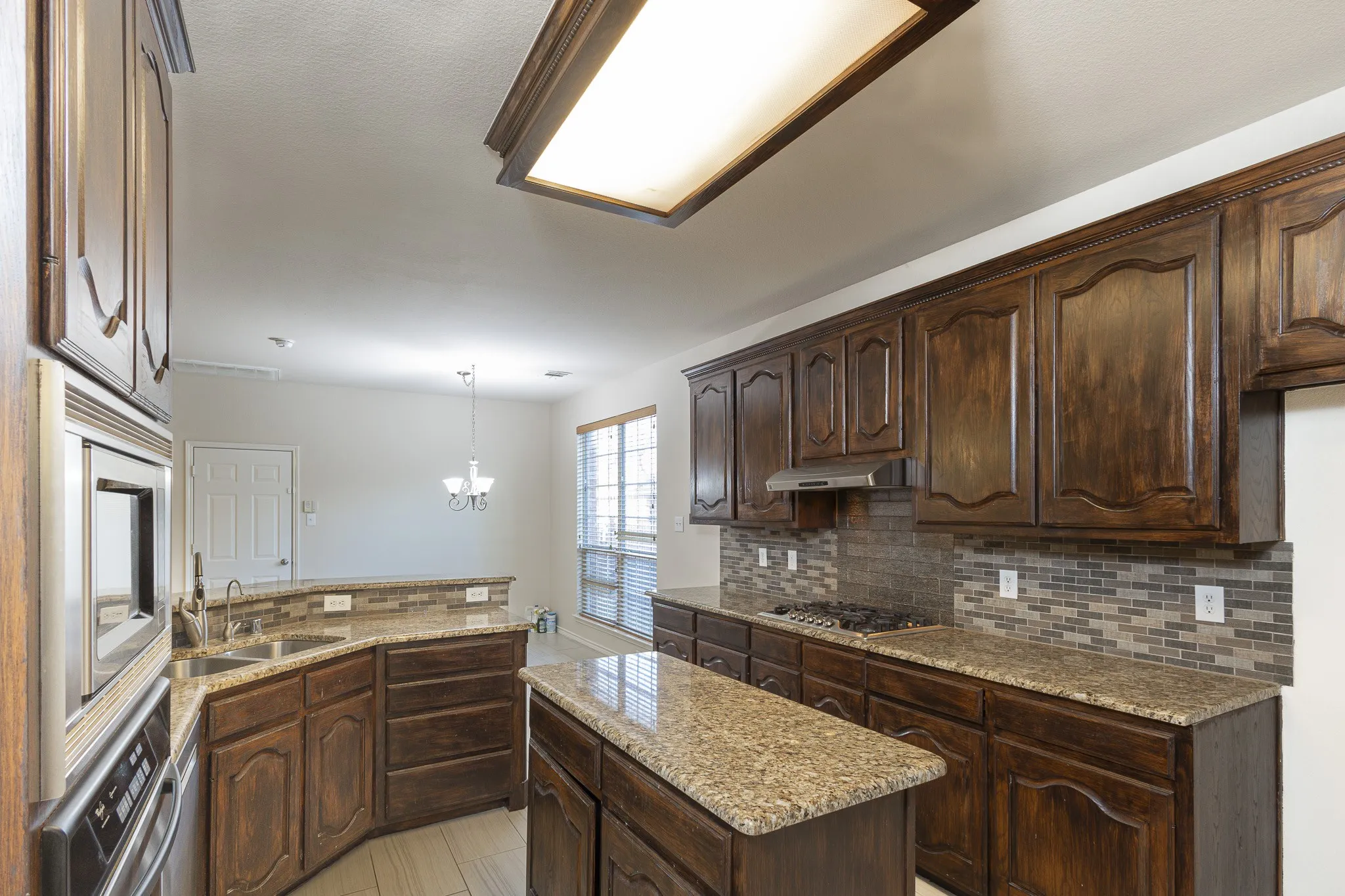 Kitchen featuring light stone countertops, decorative light fixtures, dark brown cabinetry, sink, and light tile floors