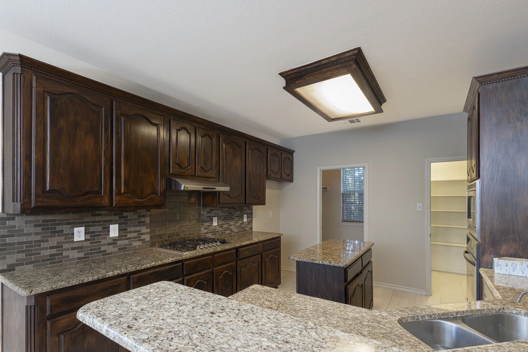 Kitchen with light stone countertops, dark brown cabinetry, a kitchen island, backsplash, and light tile floors