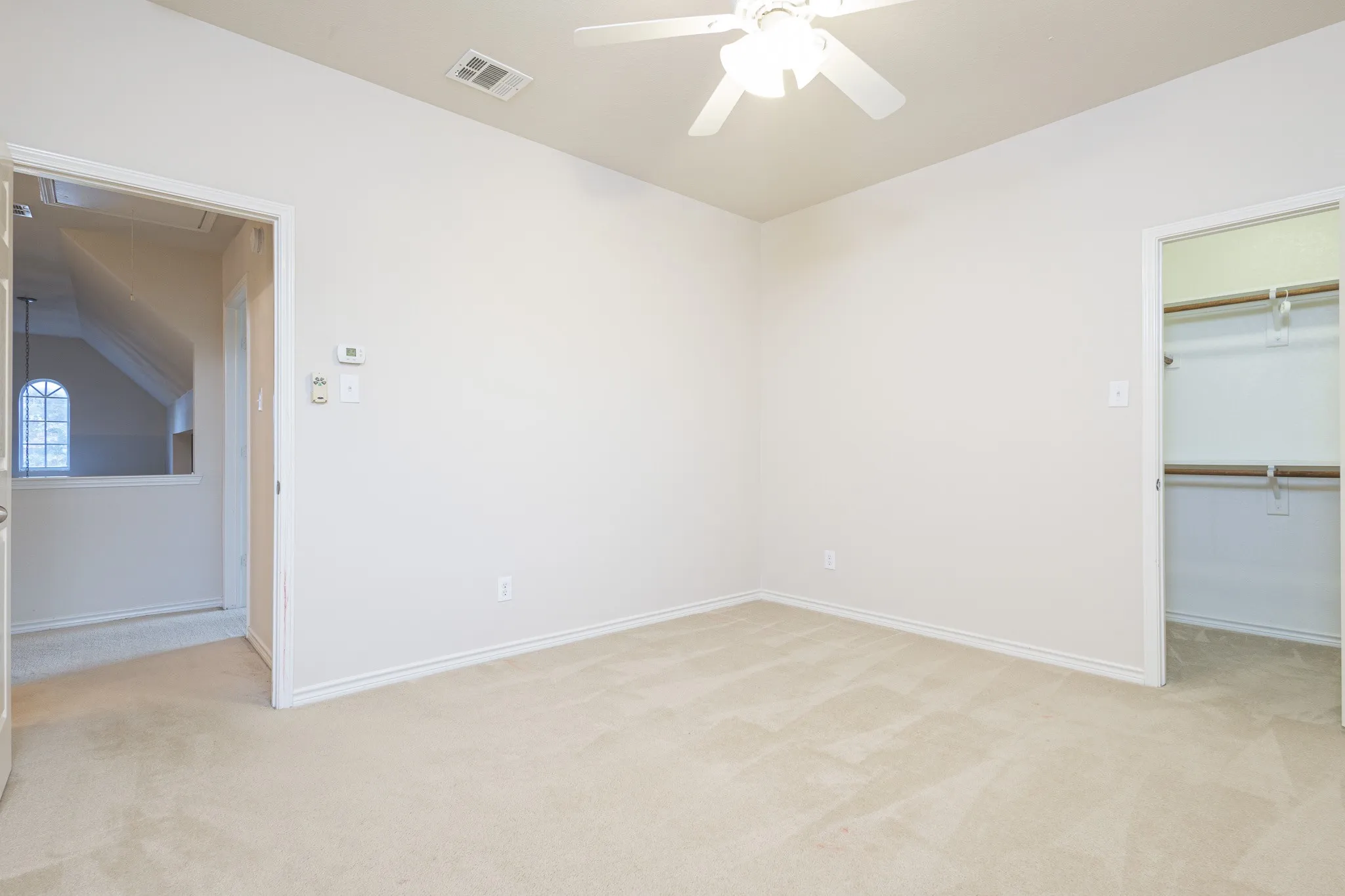 Unfurnished bedroom featuring light carpet, a spacious closet, lofted ceiling, and ceiling fan