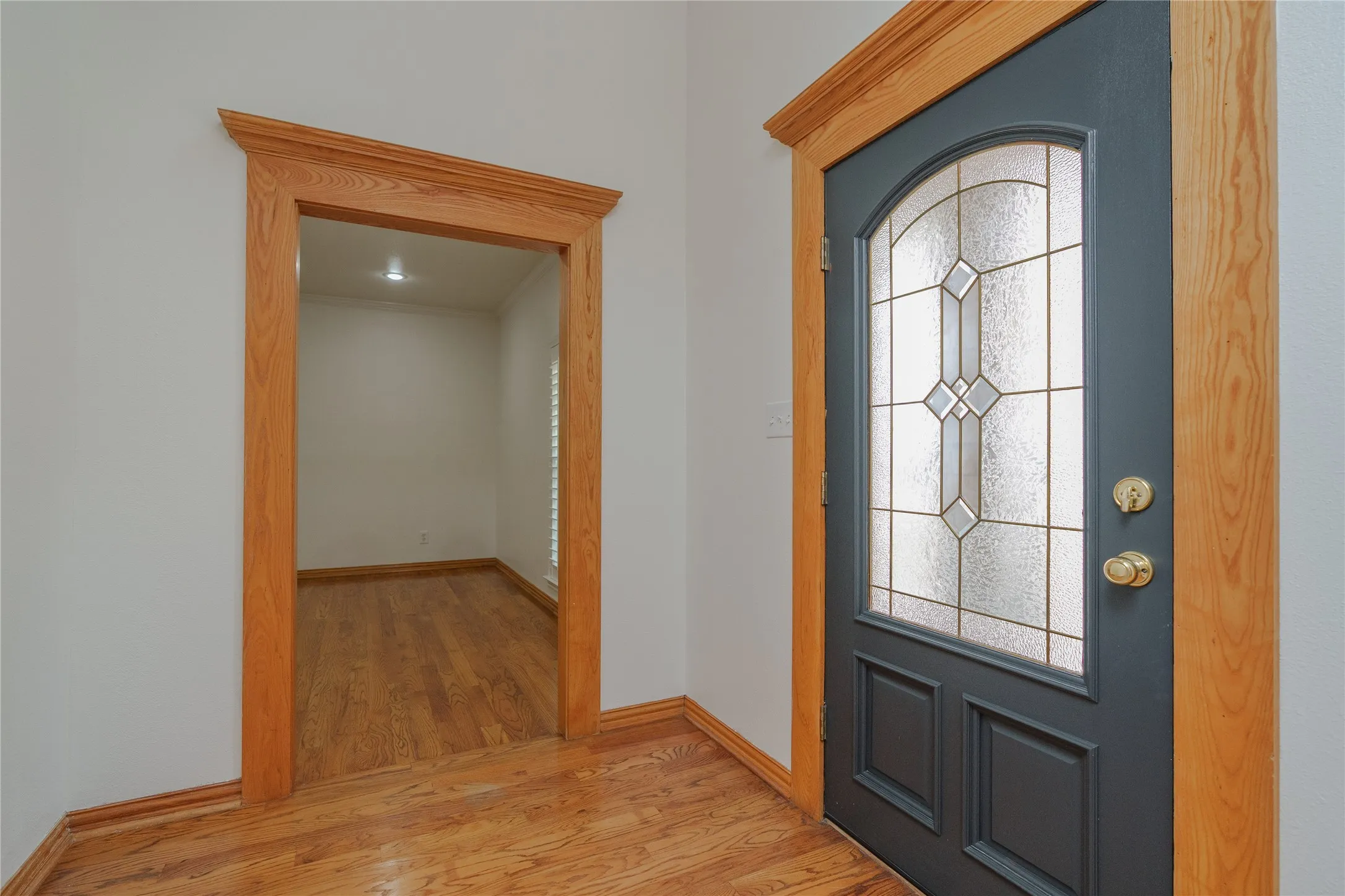 Entryway featuring a dark paneled door with decorative leaded glass, brass hardware, and natural wood-finish trim and baseboards