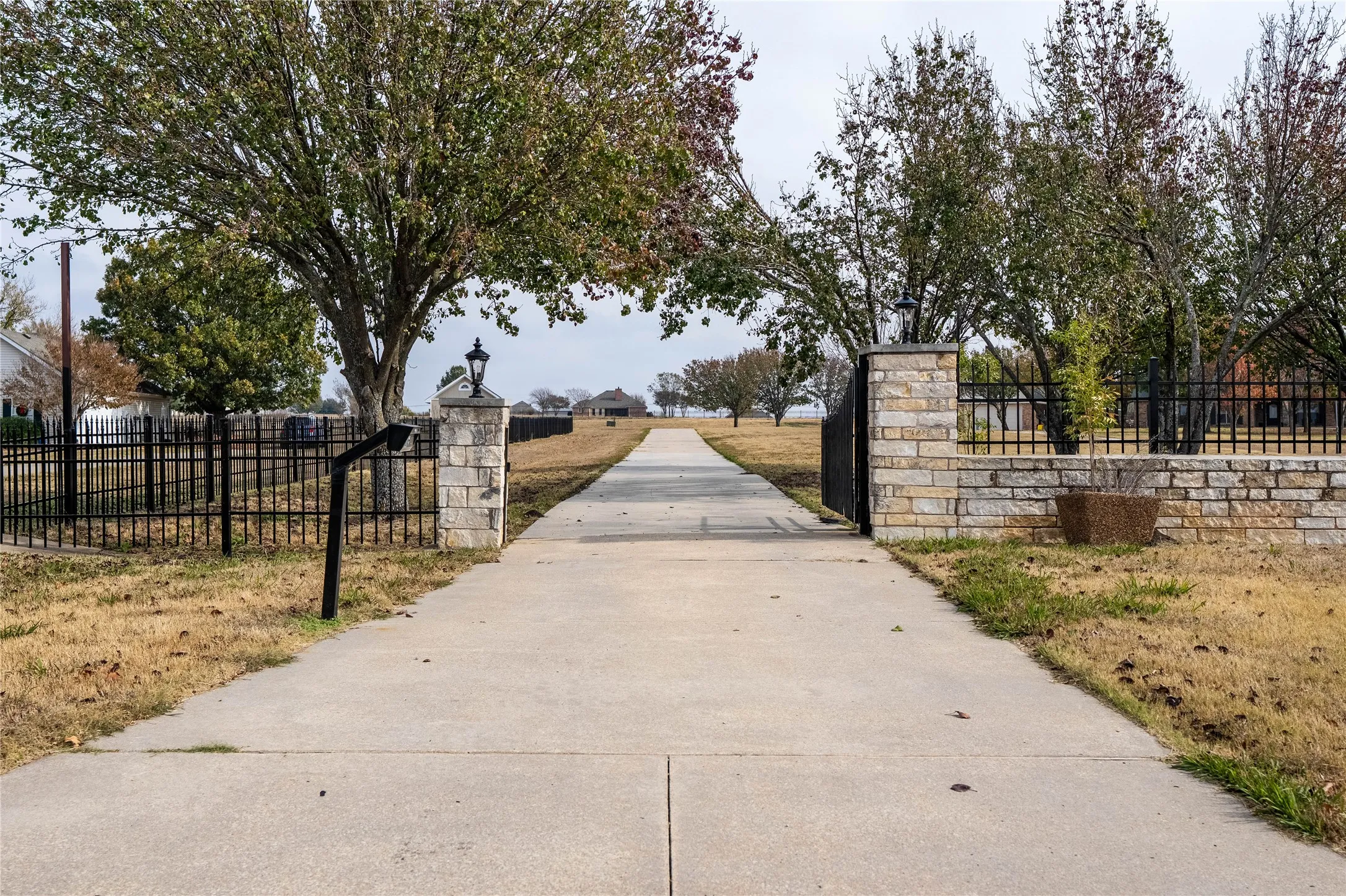 Long concrete driveway framed by stone columns with integrated lighting and black metal fencing