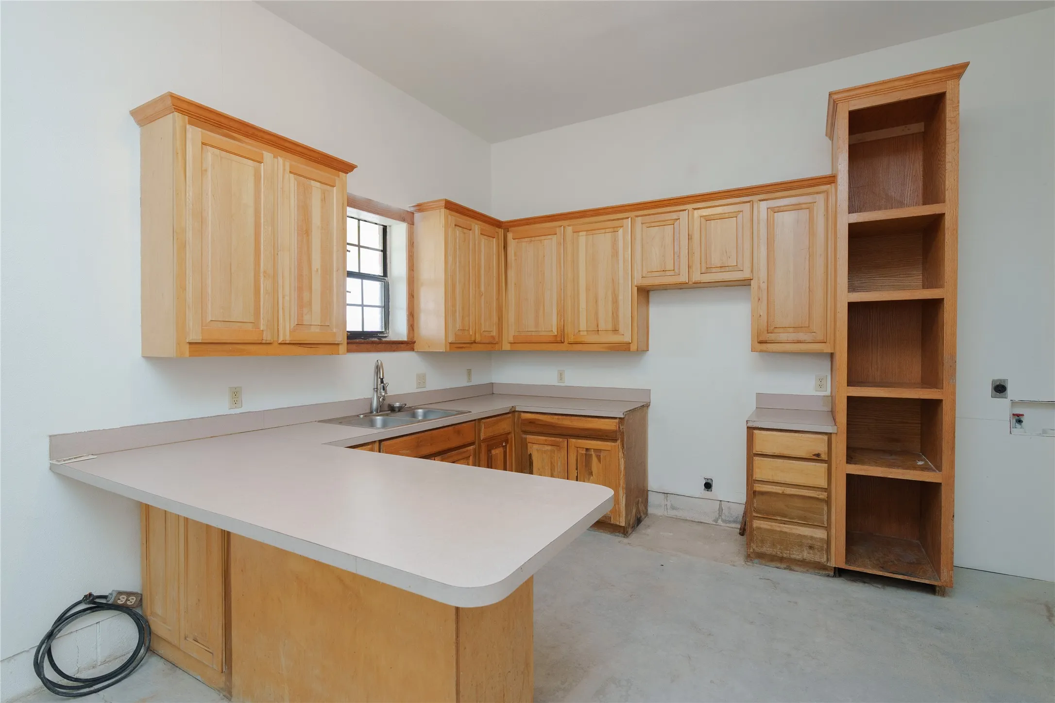 Kitchen space in the secondary garage, featuring natural wood cabinetry, built-in shelving, a double basin sink with a chrome faucet, and light-toned countertops