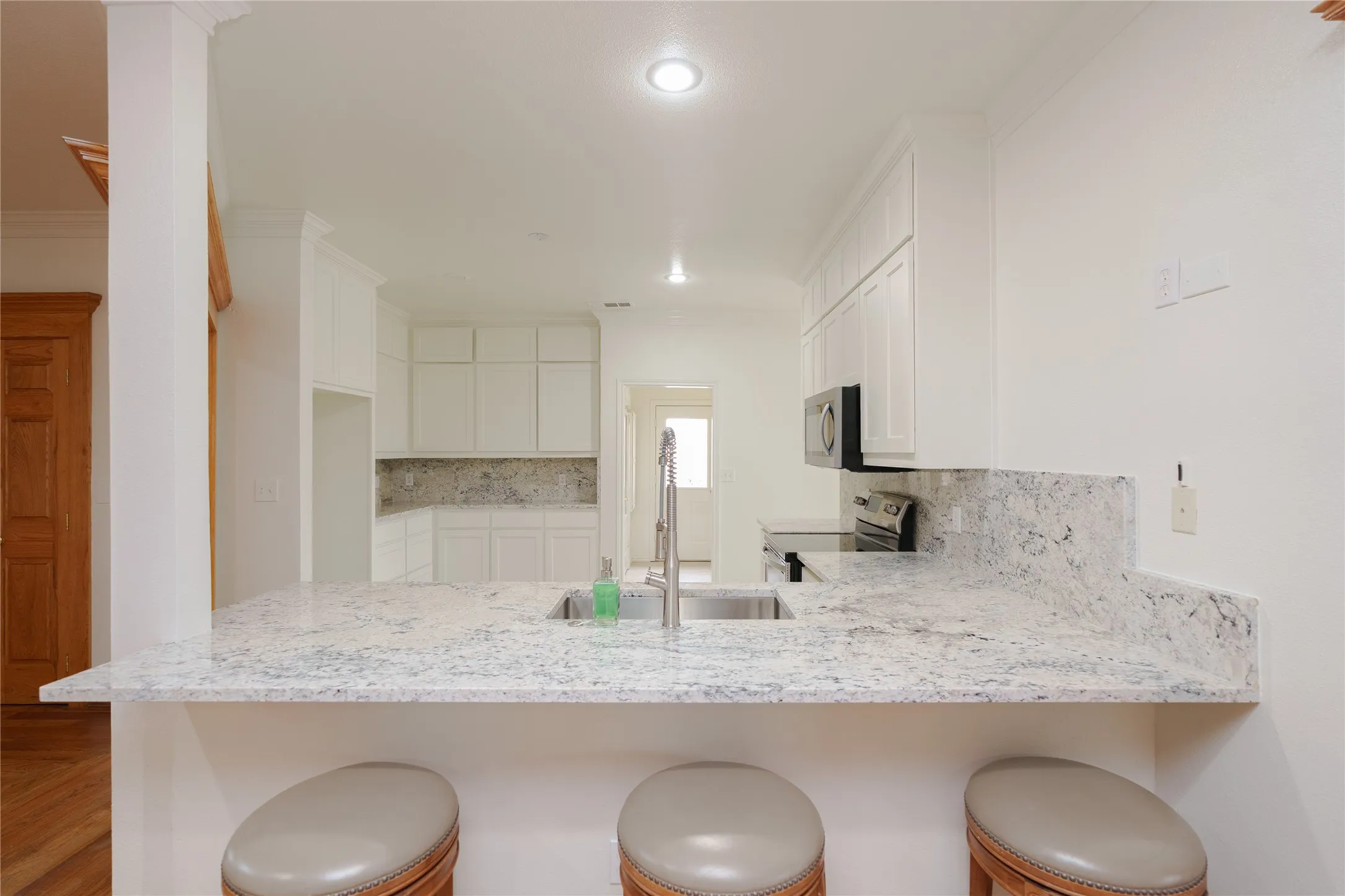 Kitchen featuring a spacious bar with seating, a stainless steel undermount sink, white cabinetry, integrated stainless steel appliances, recessed lighting, and stone countertops