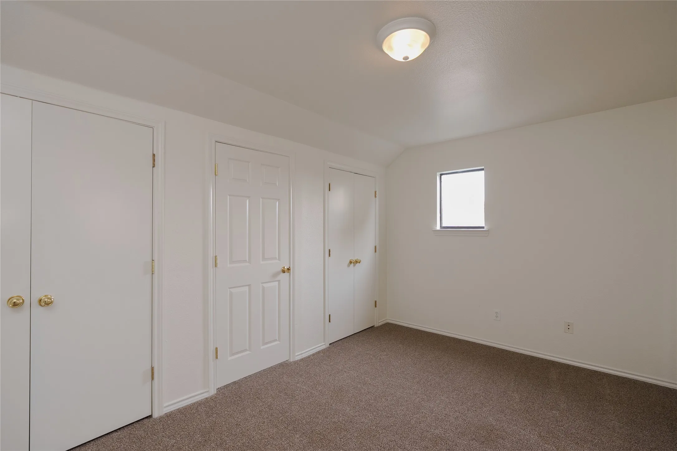 Carpeted interior space featuring multiple white panel doors with brass hardware, a single window, and a flush-mount ceiling light fixture