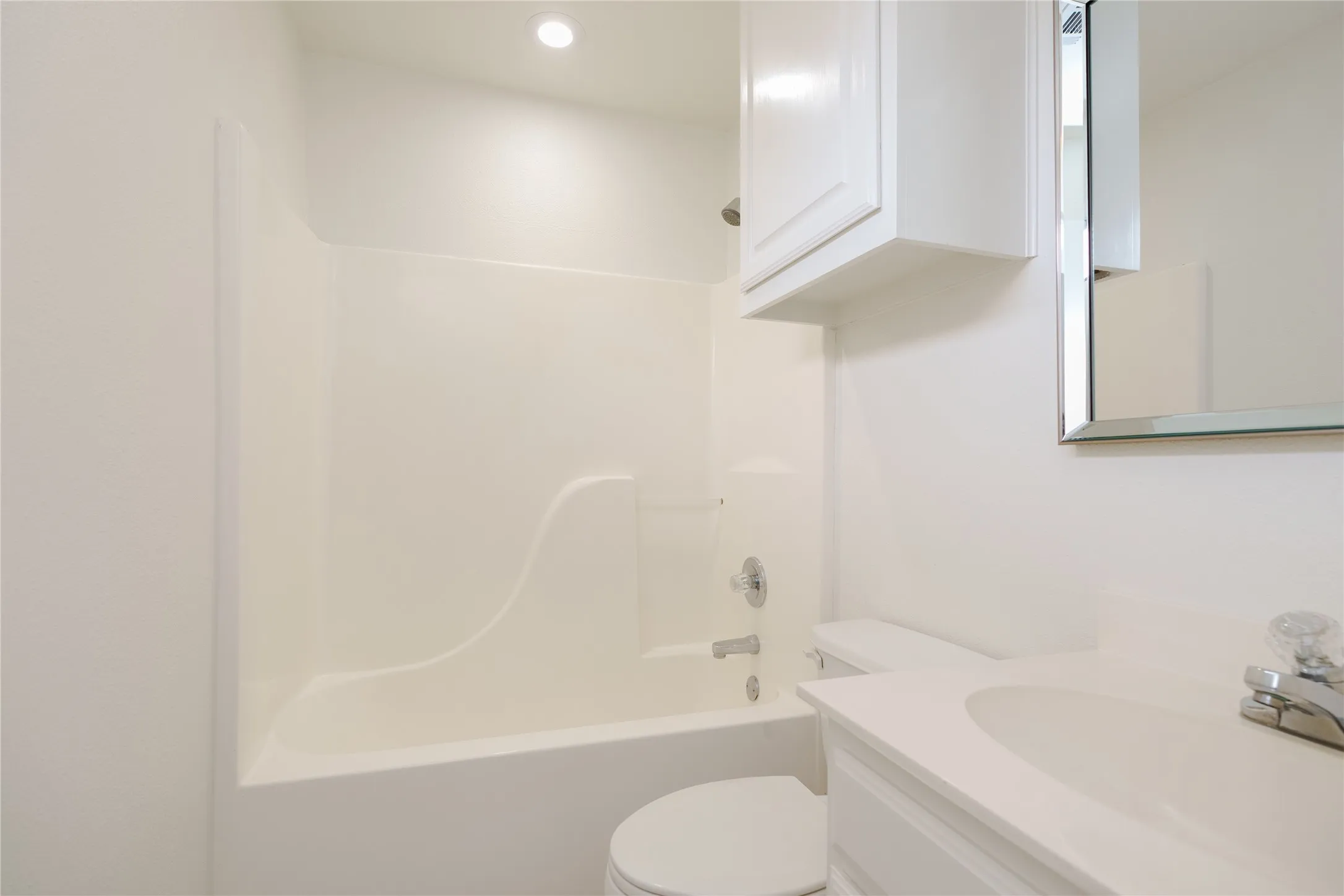 Second primary suite Bathroom, featuring a white integrated tub and shower unit, a white vanity with an integrated sink, a mirrored medicine cabinet, a wall-mounted cabinet, and recessed ceiling lighting