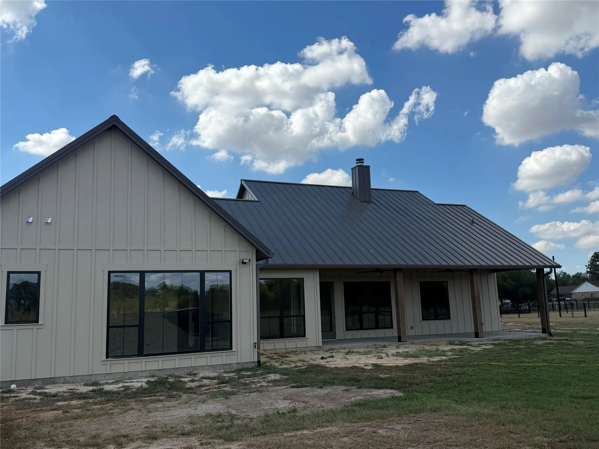 Board and batten siding, dark metal roofing, black-framed windows, and an expansive covered patio
