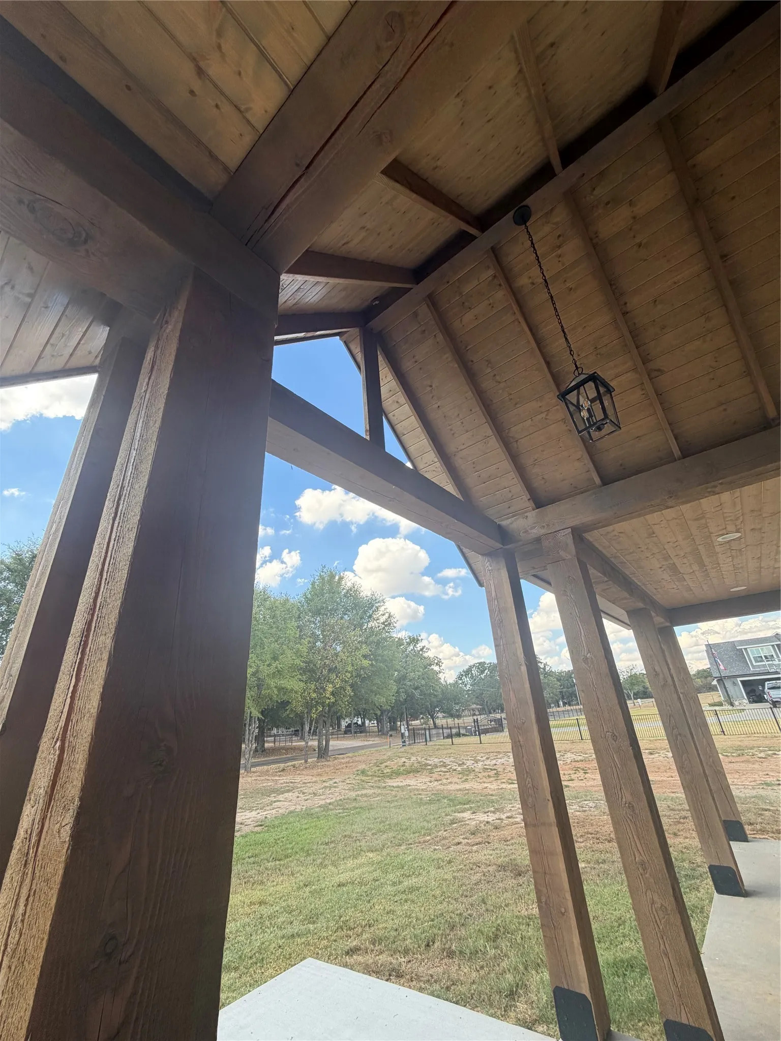 Exposed wood-finish beams and ceiling panels, vaulted porch ceiling, suspended lantern-style light fixture, and concrete porch flooring