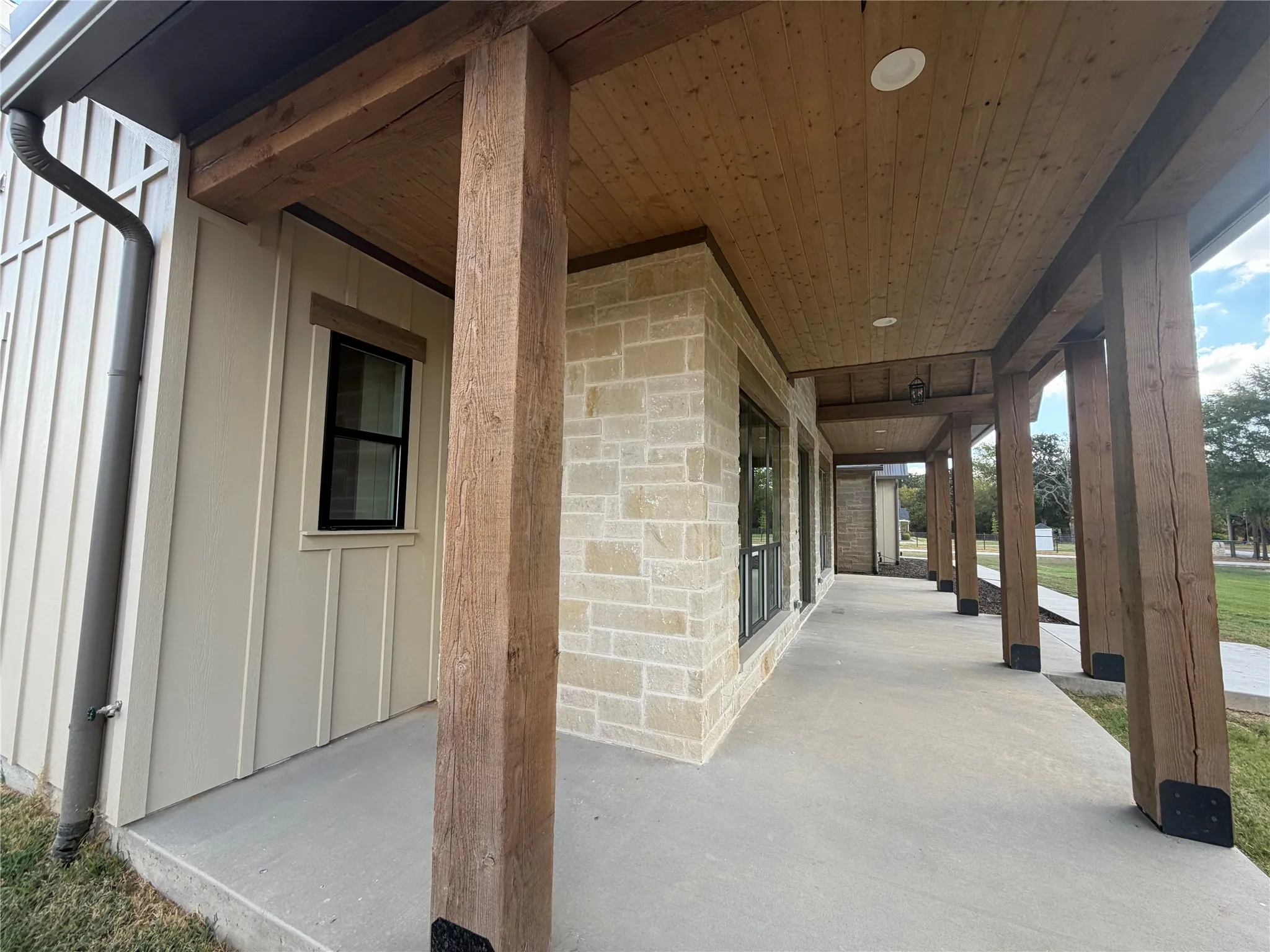Stone and vertical panel siding exterior with a wood-finish porch ceiling and exposed wood beams