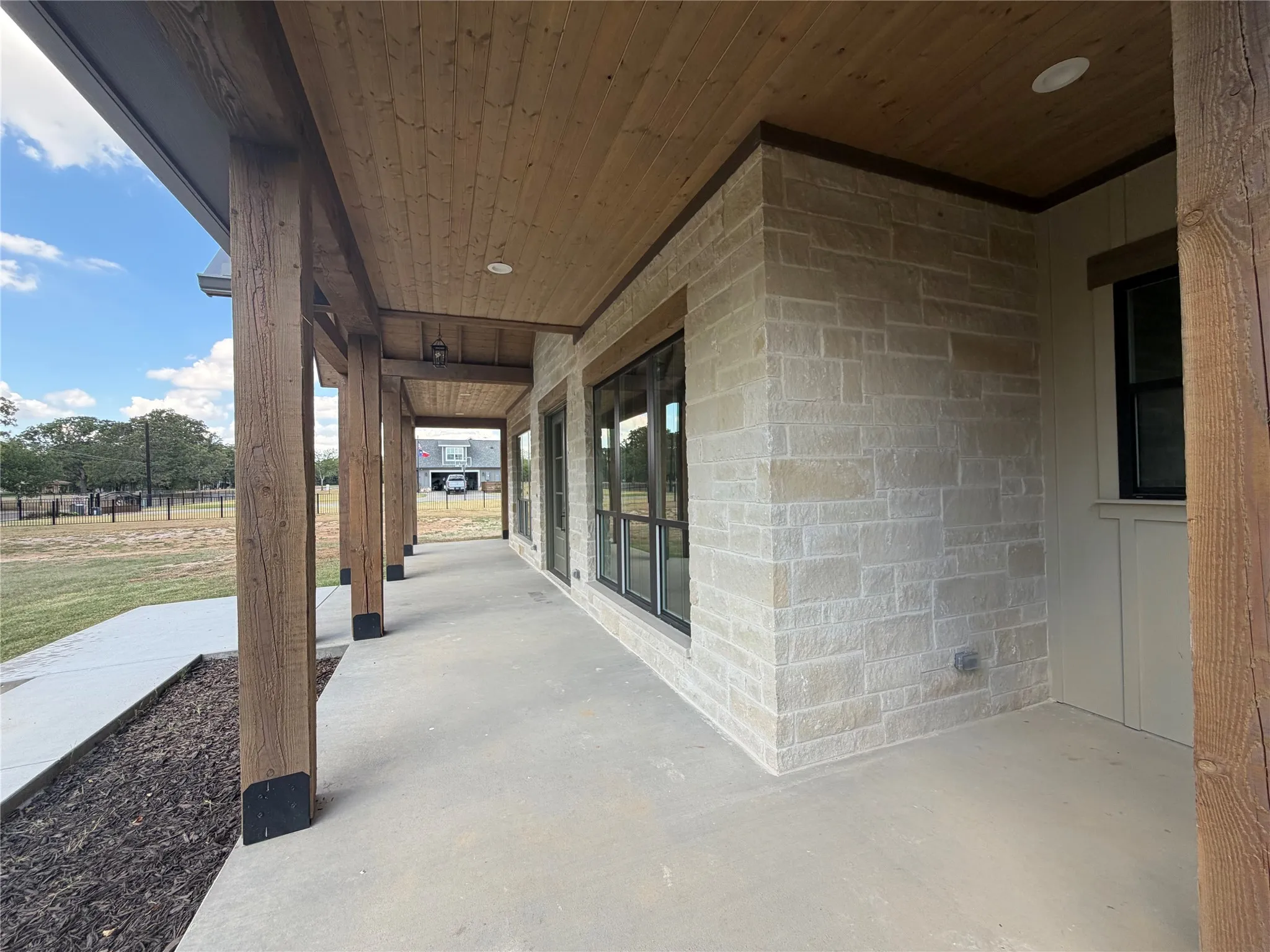 Expansive covered porch with wood-finish ceiling, exposed wood beams, concrete flooring, and stone facade
