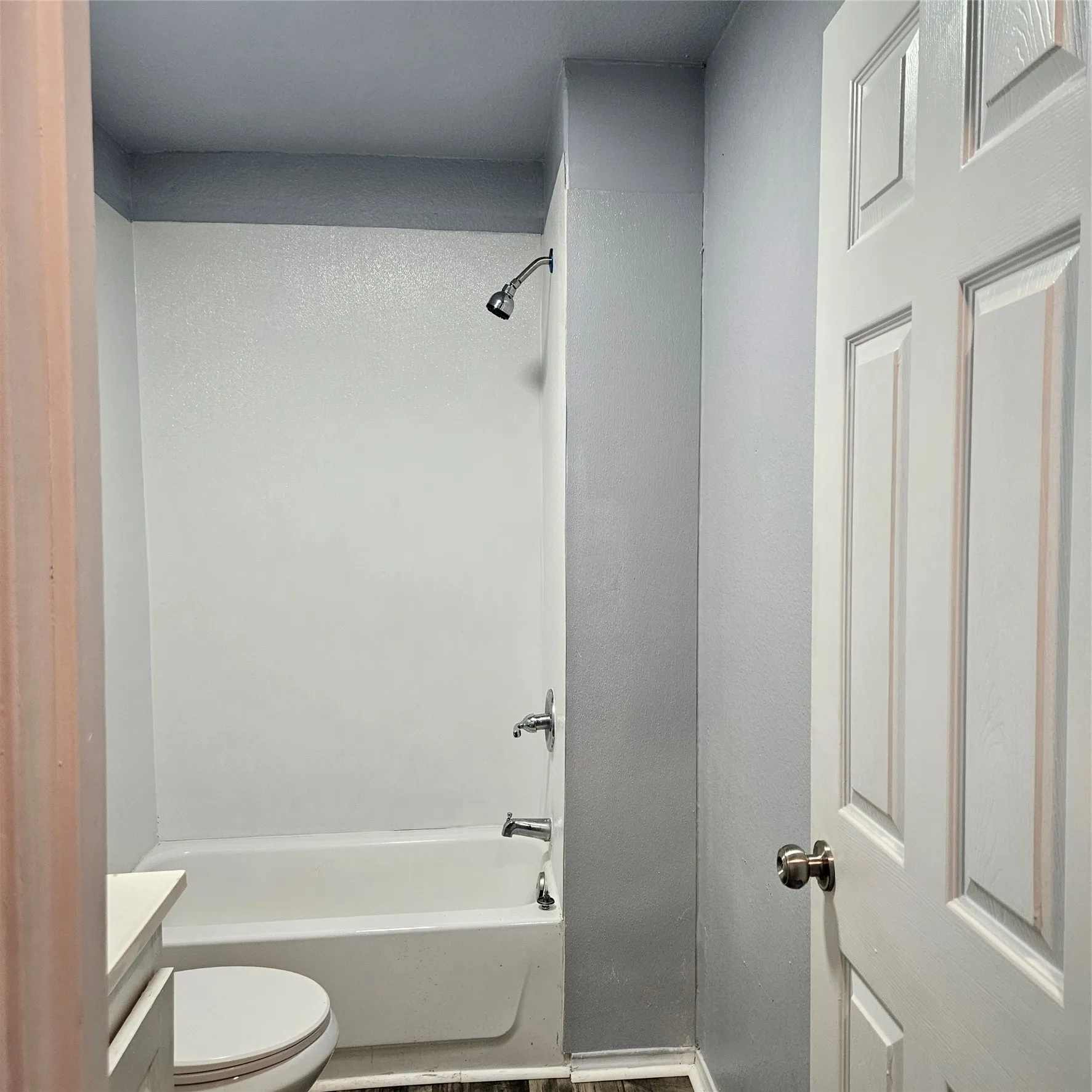 Bathroom featuring a white bathtub with integrated shower, chrome fixtures, and a privacy door