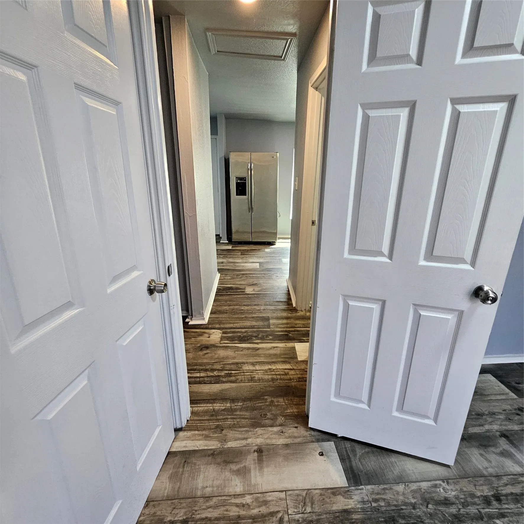 Hallway featuring wood-finish flooring, light gray wall paint, white trim, and white paneled doors