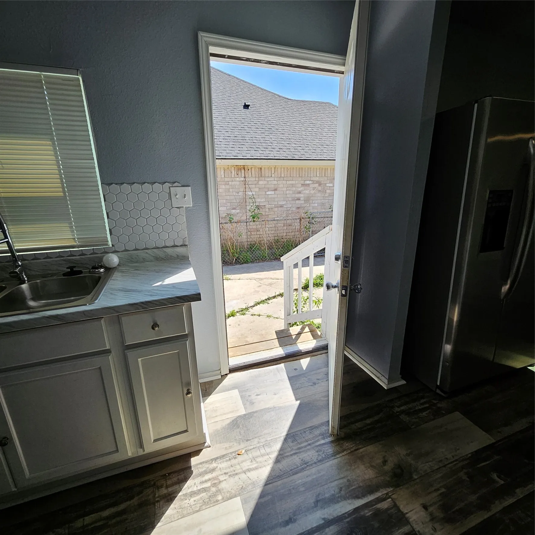 Kitchen area featuring wood-finish flooring, white cabinetry, a double basin sink, and hexagonal tile backsplash