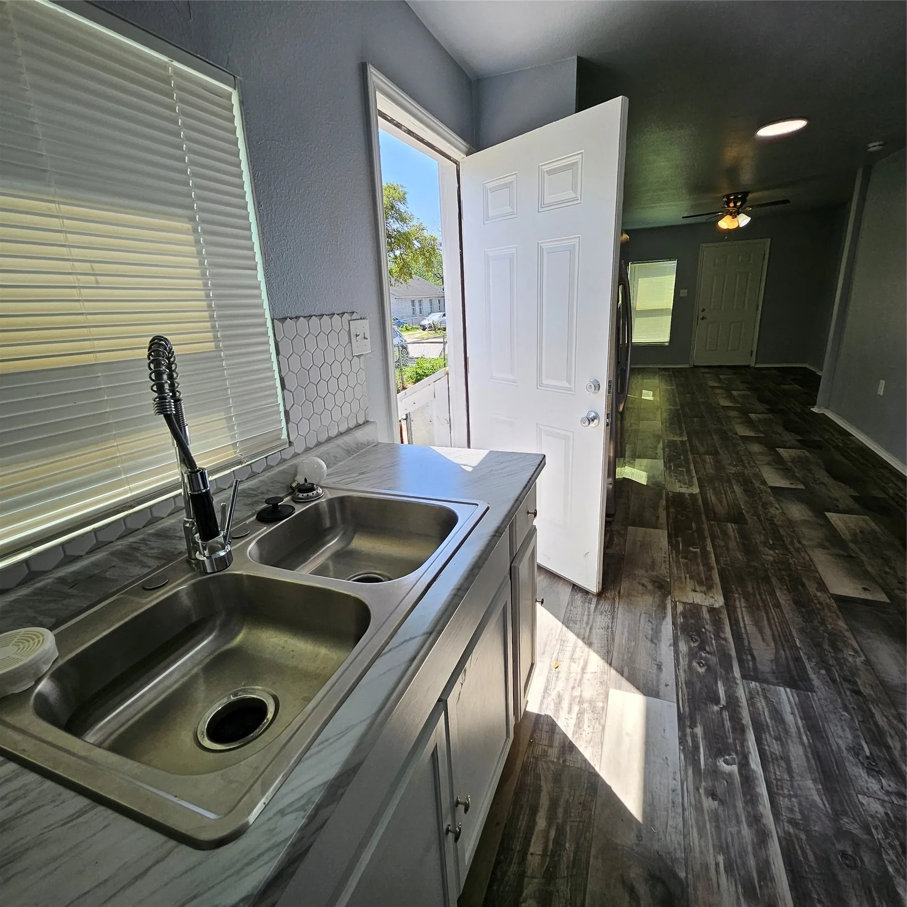 Kitchen area featuring a double basin stainless steel sink with a high-arc faucet, honeycomb tile backsplash, and light-toned cabinetry