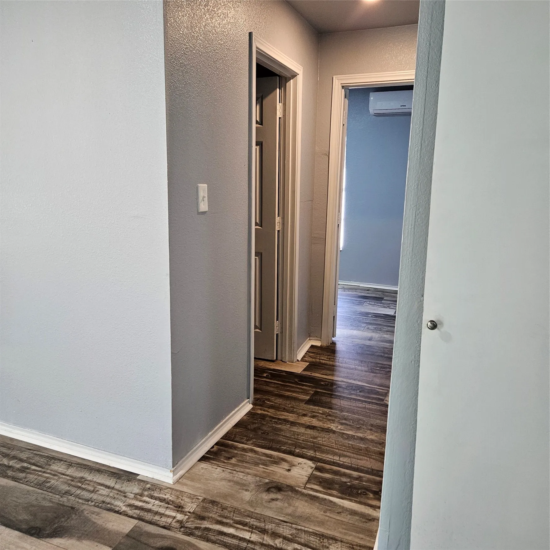 Wood-finish flooring extending through a hallway with light gray walls and white trim