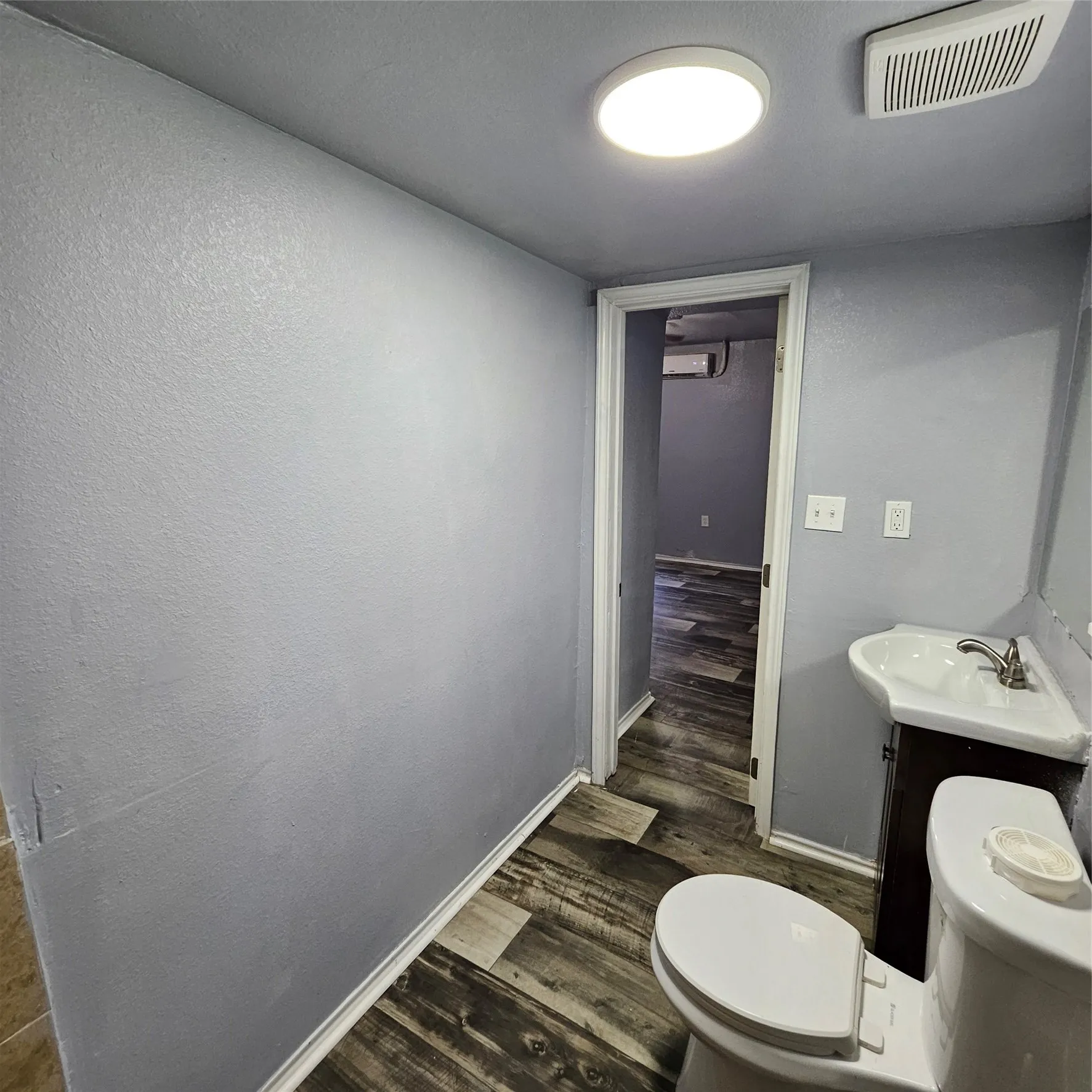 Bathroom featuring wood-finish flooring, a white toilet, and a pedestal sink with dark wood-finish cabinetry