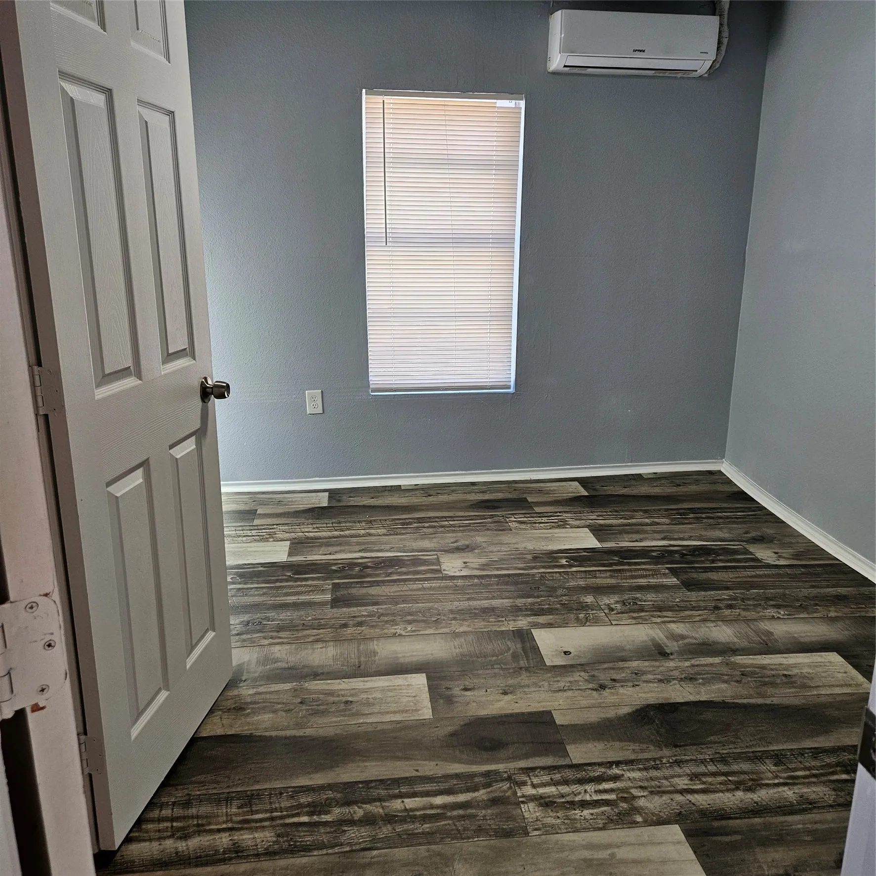 Room featuring wood-finish flooring, a window with blinds, and a wall-mounted air conditioning unit