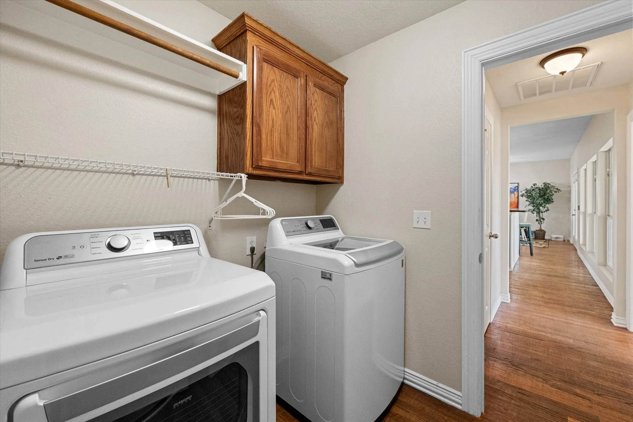 Dedicated laundry area featuring wood-finish flooring, overhead cabinetry, and a white wire shelf with hanging rod
