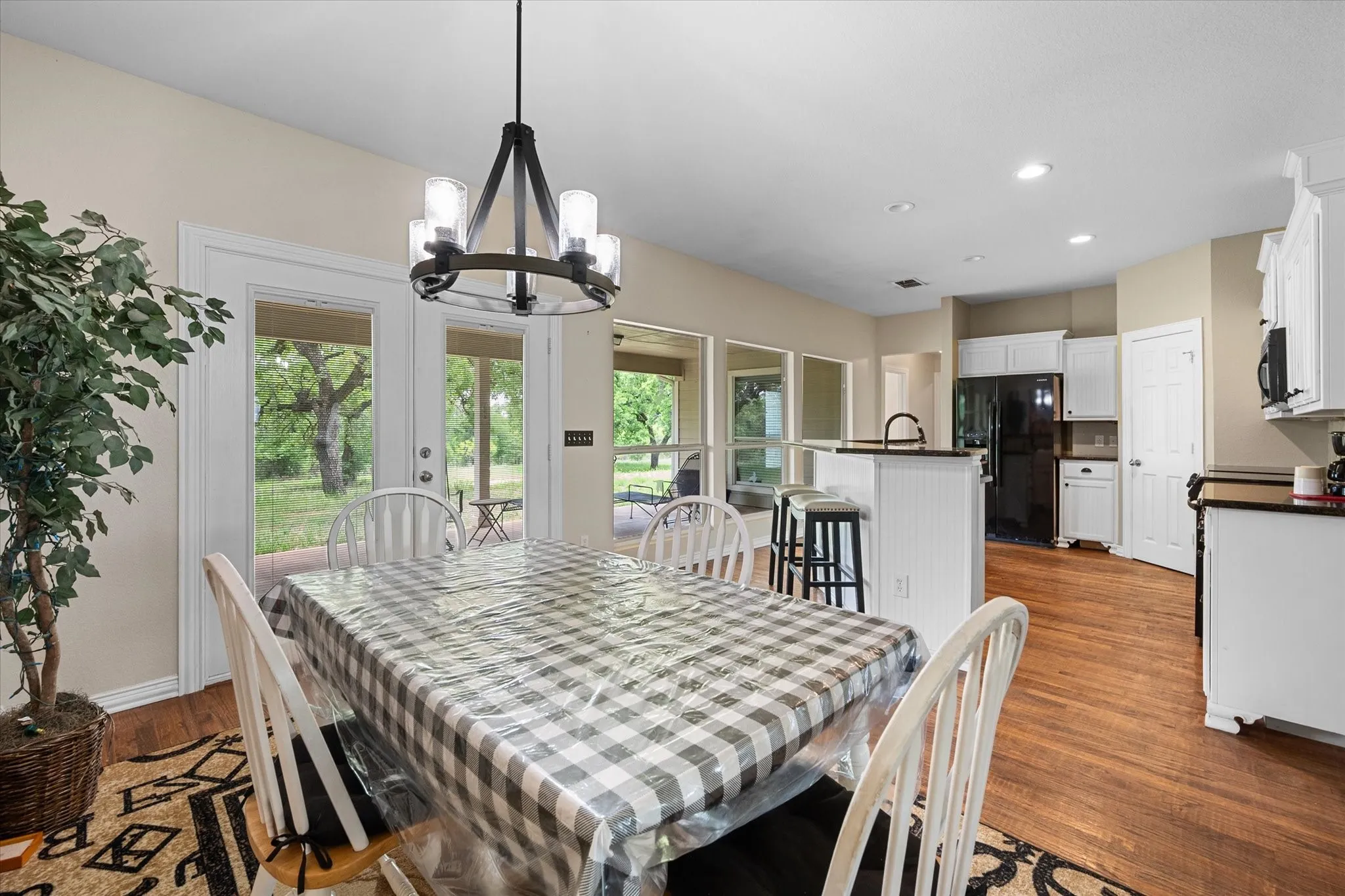 Dining area with wood-finish flooring, featuring a modern chandelier and double glass-paneled doors opening to an exterior patio