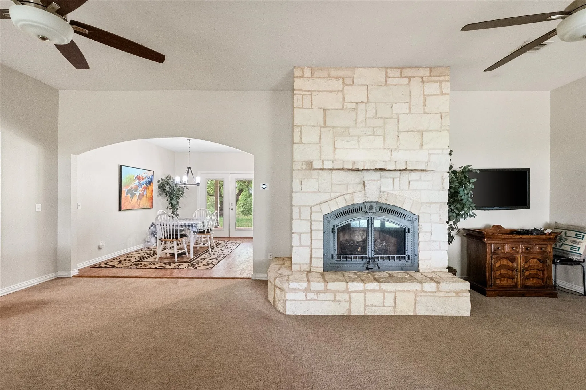 Living area featuring a stone-clad fireplace with an insert, carpet flooring, and ceiling fans