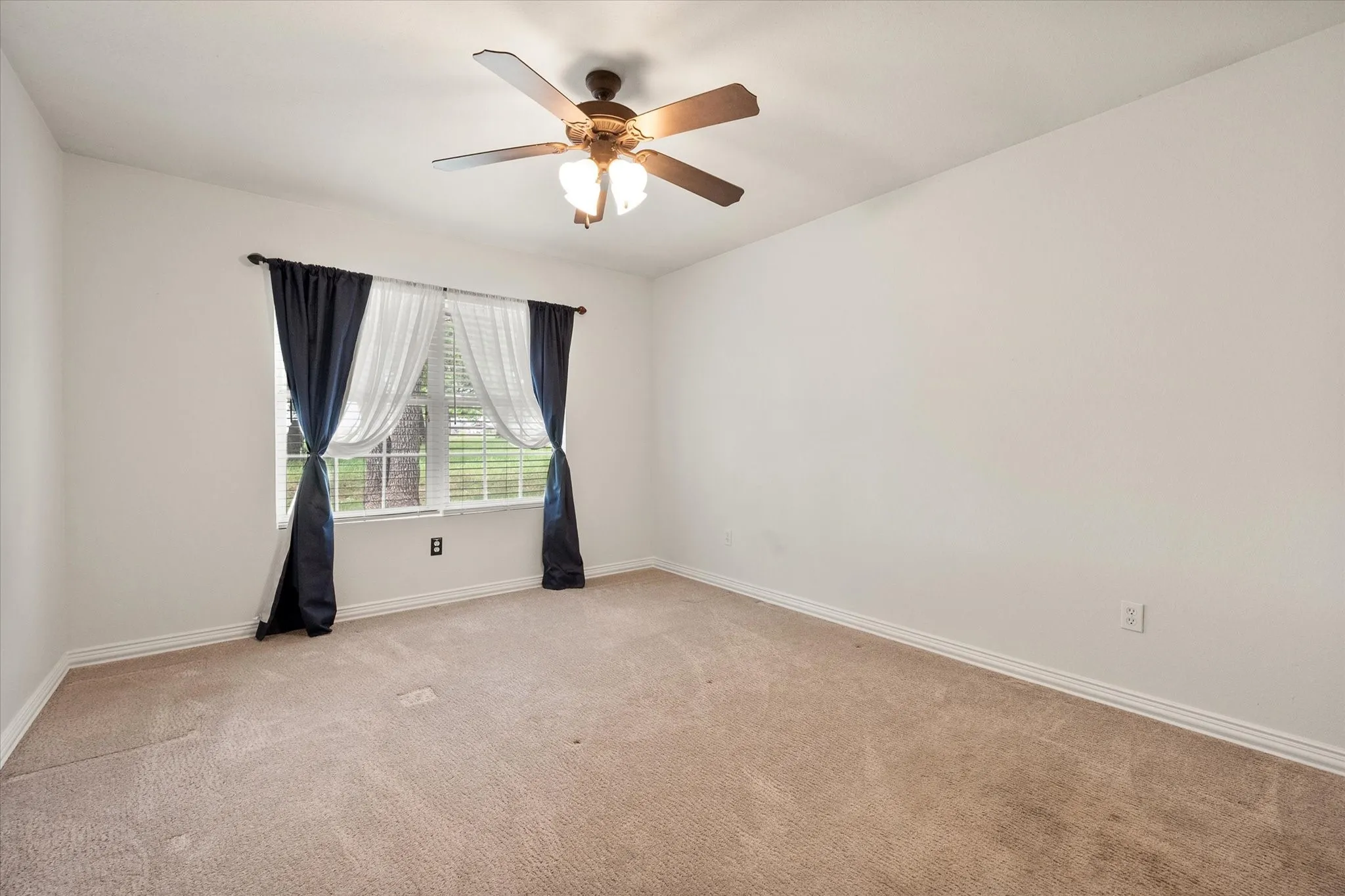 Carpeted room featuring a window with blinds, a ceiling fan with integrated lighting, and white baseboards