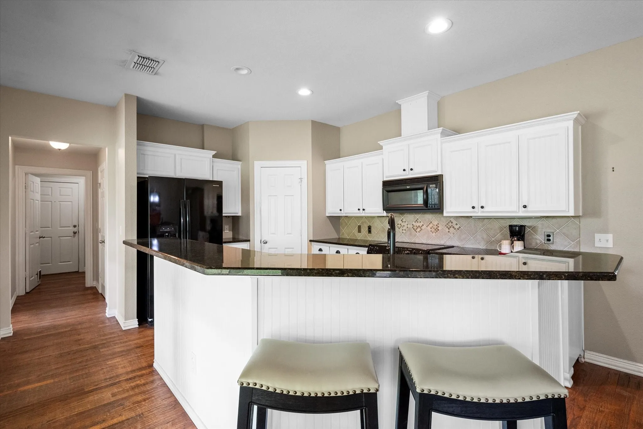 Kitchen featuring a large breakfast bar with white beadboard paneling, dark stone countertops, white cabinetry, and a black appliance suite