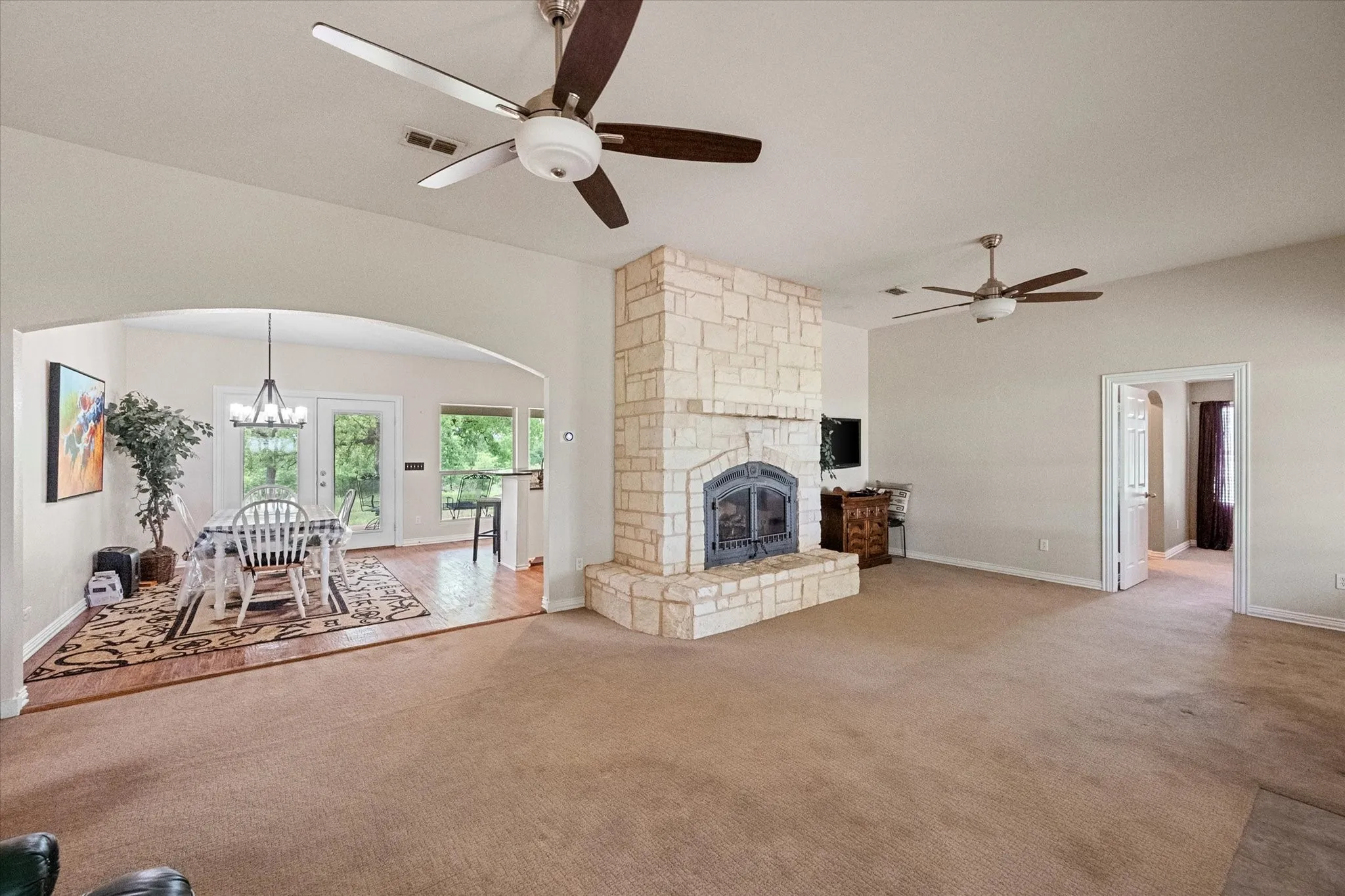 Spacious living area featuring a stone fireplace with hearth, arched doorway to dining space, and two ceiling fans