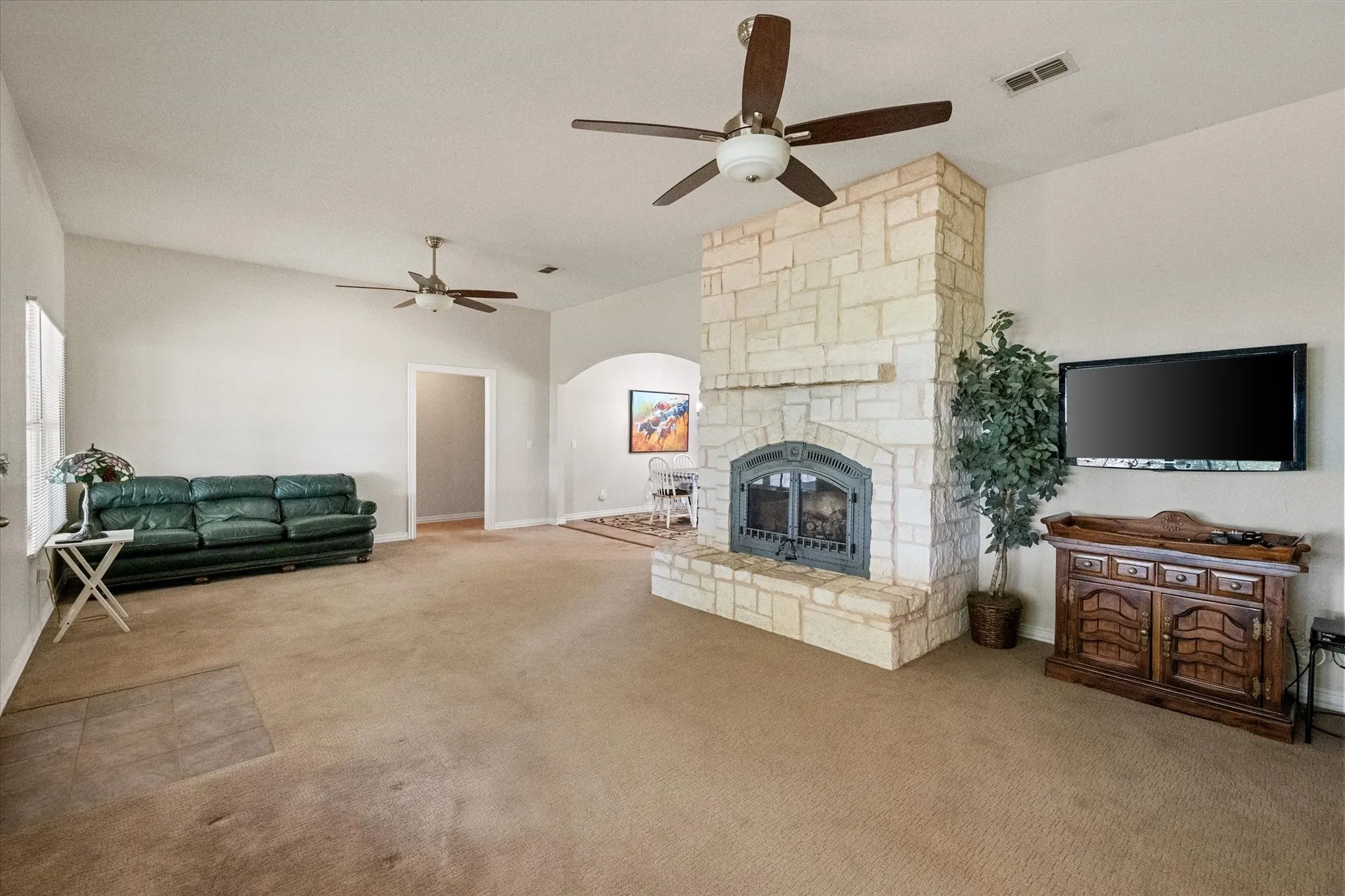 Spacious living area featuring a stone-clad fireplace with an arched firebox, multiple ceiling fans with integrated lighting, and vaulted ceilings