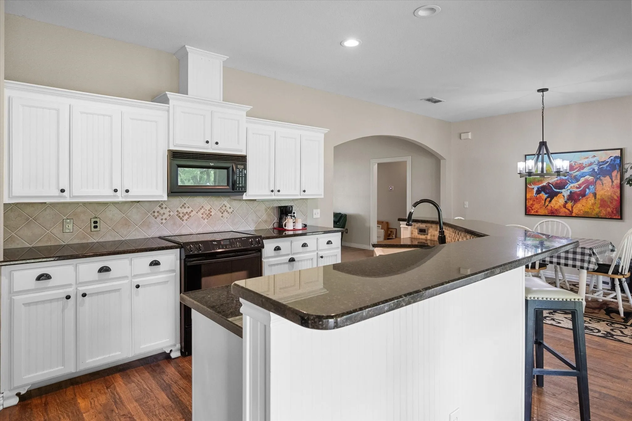 Kitchen featuring white cabinetry, dark countertops, a tile backsplash, wood-finish flooring, and a breakfast bar with beadboard paneling