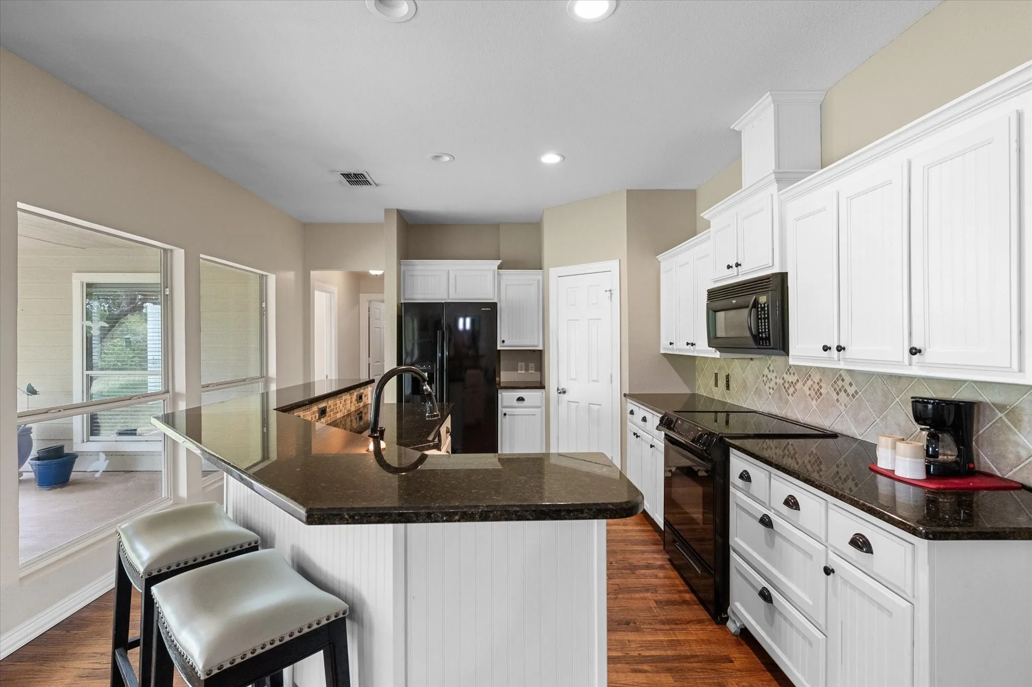 Modern kitchen featuring white cabinetry, dark countertops, a large island with a built-in sink, stainless steel appliances, and wood-finish flooring