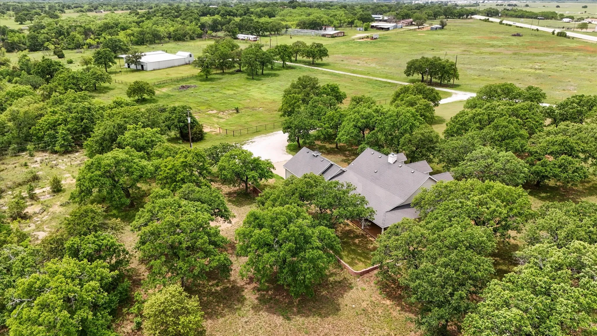 Expansive property featuring a modern roofline, a gravel driveway, mature trees, and a surrounding natural landscape
