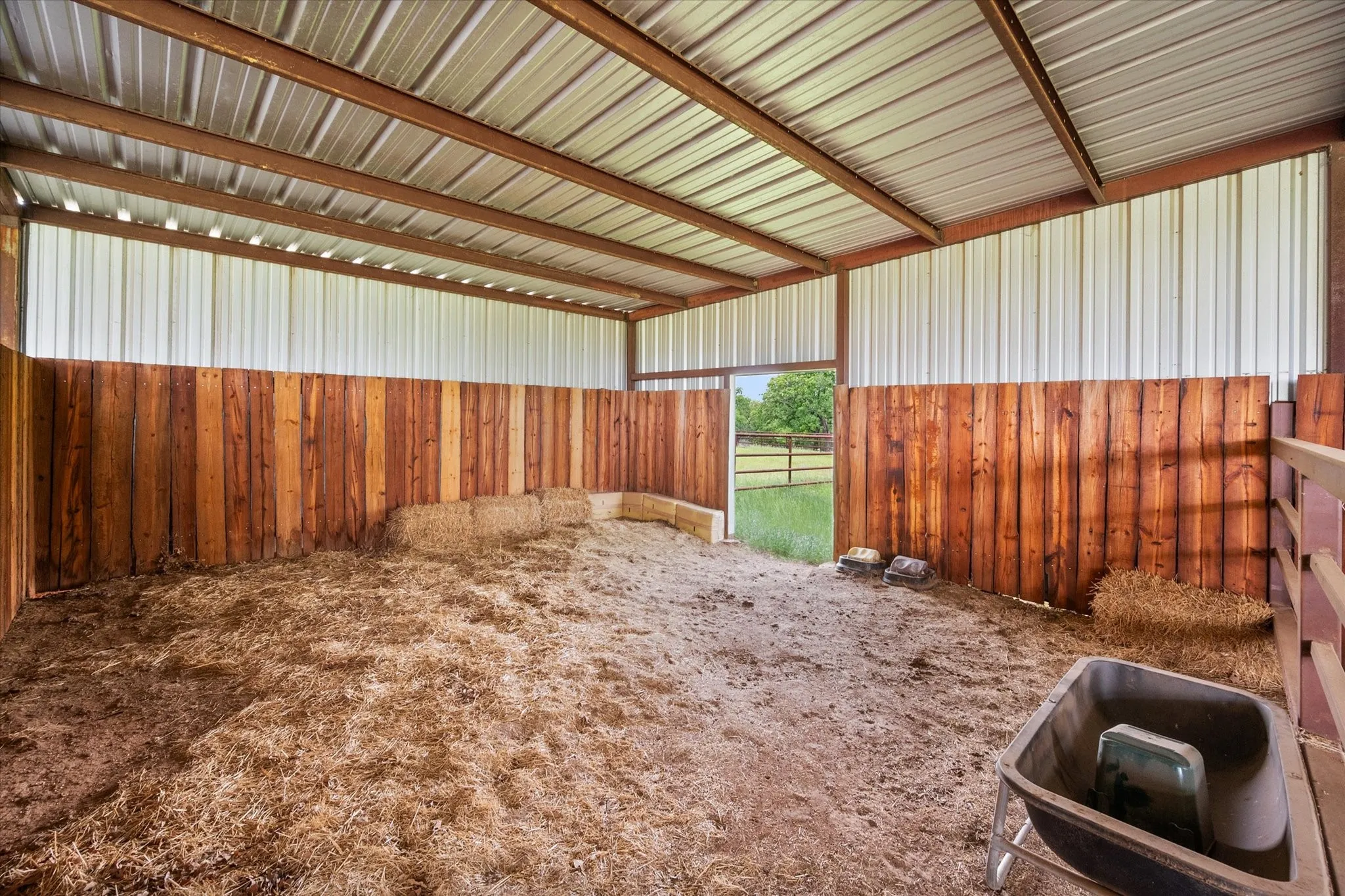 Open-air barn structure featuring a corrugated metal roof, exposed metal beams, and vertical wood plank walls