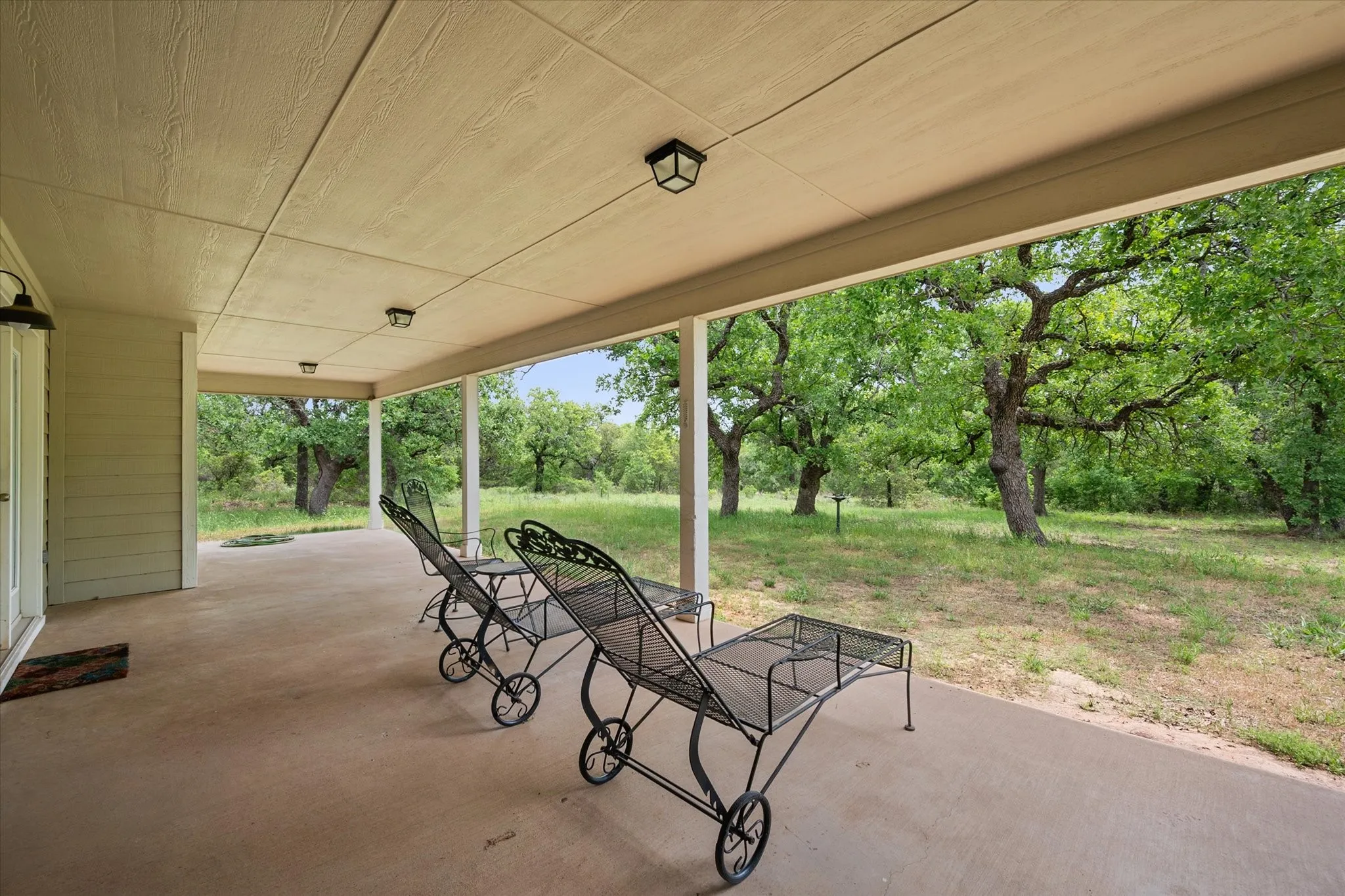 Spacious covered patio with concrete flooring, recessed lighting, and expansive tree-lined surroundings