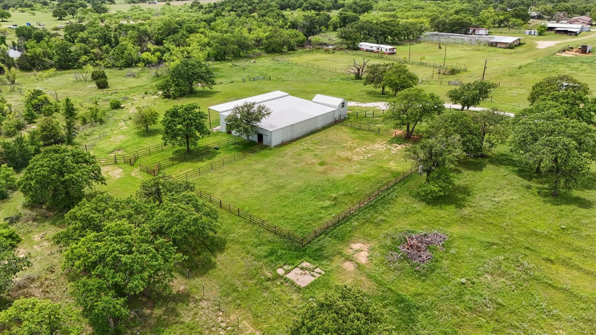 Expansive property featuring a large metal building with an attached covered porch, surrounded by lush green landscaping