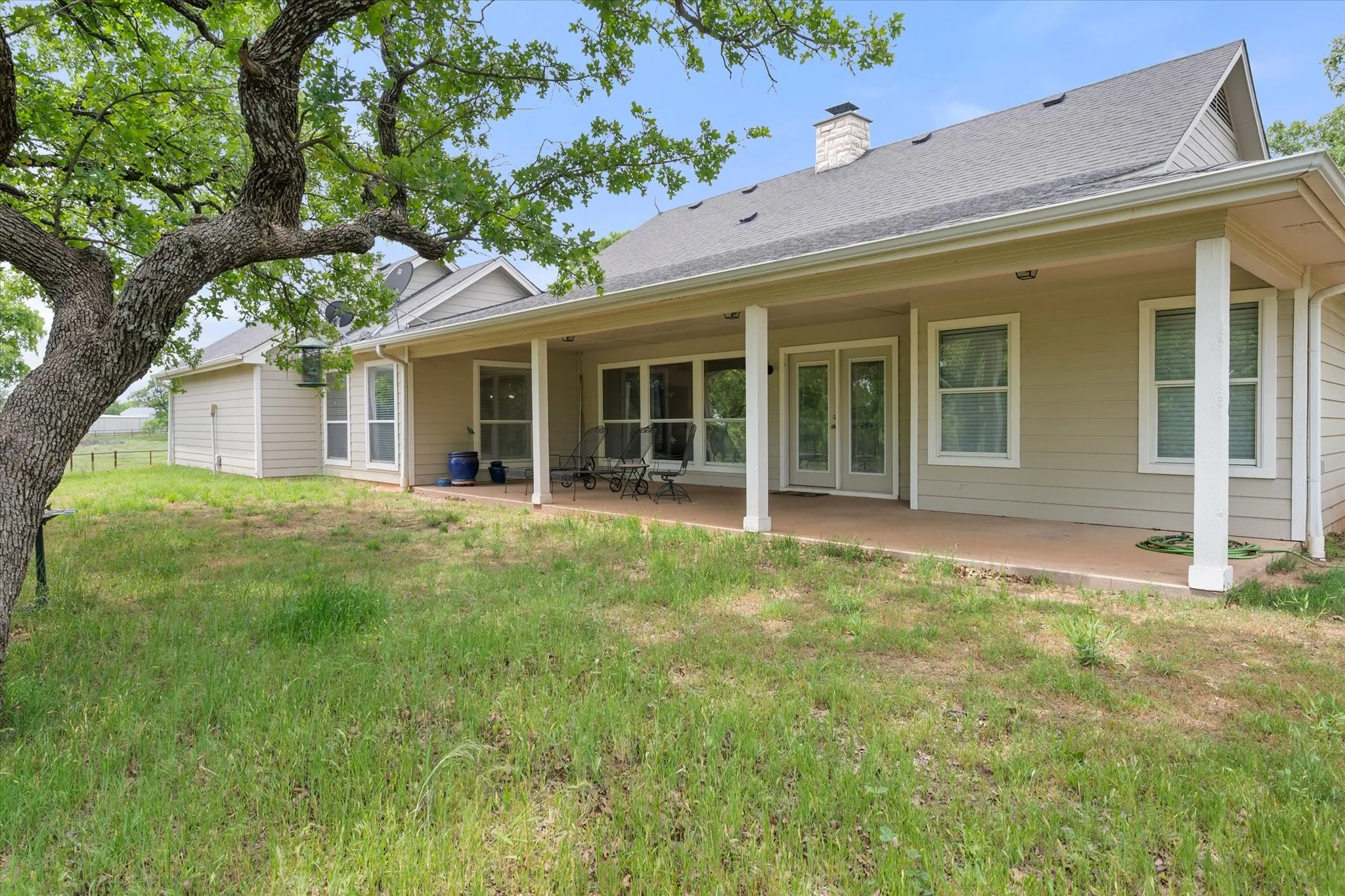 Expansive backyard featuring a covered patio, multiple large windows, and mature trees