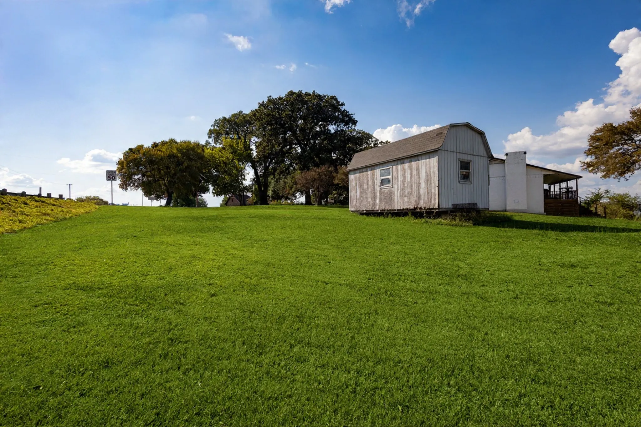 Expansive green lawn with a white wood-sided outbuilding featuring a gambrel roof and multiple windows