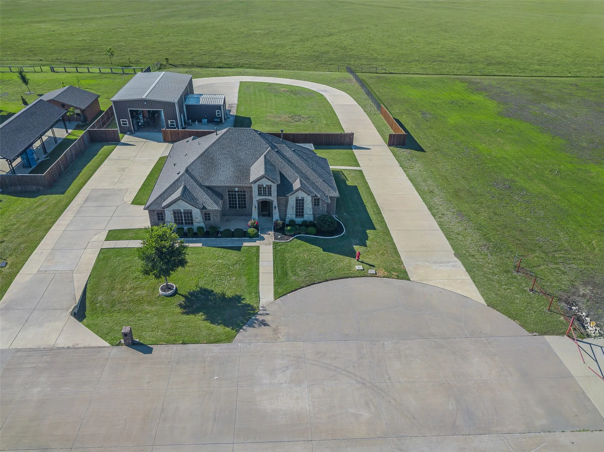 Expansive property featuring a large residence with a brick and stone facade, a multi-car detached garage, a covered carport, and extensive concrete driveways