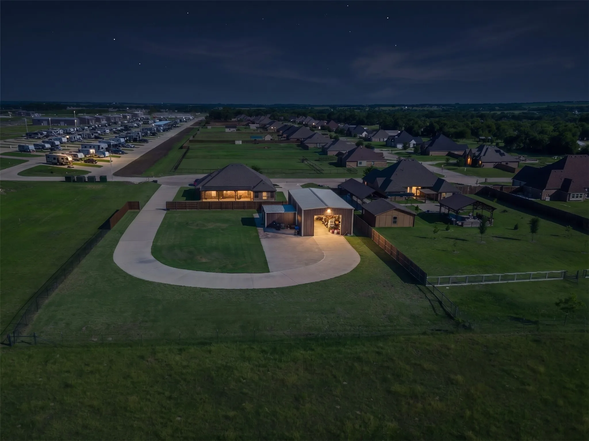 Spacious property featuring a large metal workshop building with interior lighting, an expansive paved driveway, and a fenced backyard