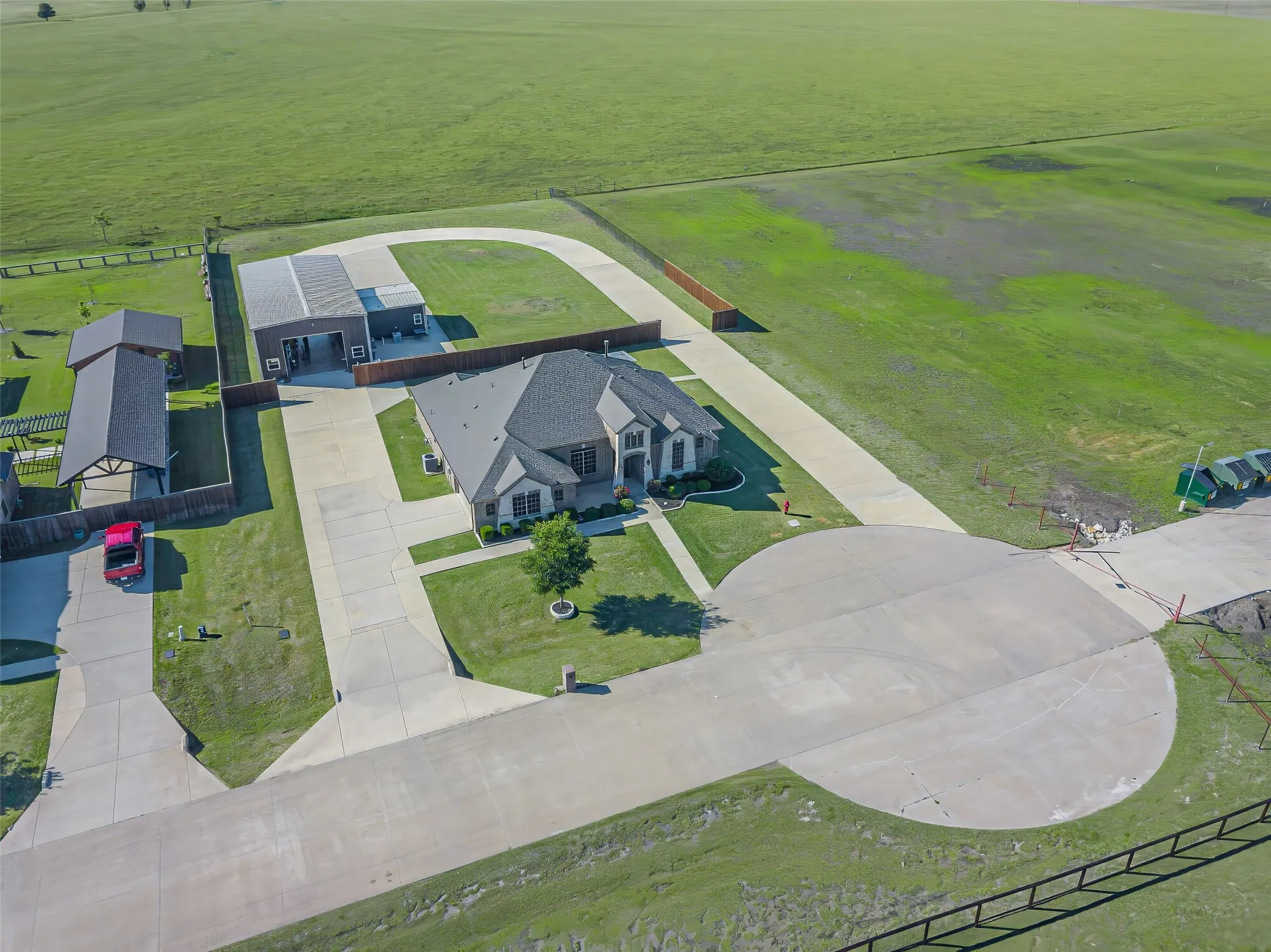 Expansive property featuring a large residence, separate outbuilding, covered carport, concrete driveways, and surrounding green spaces