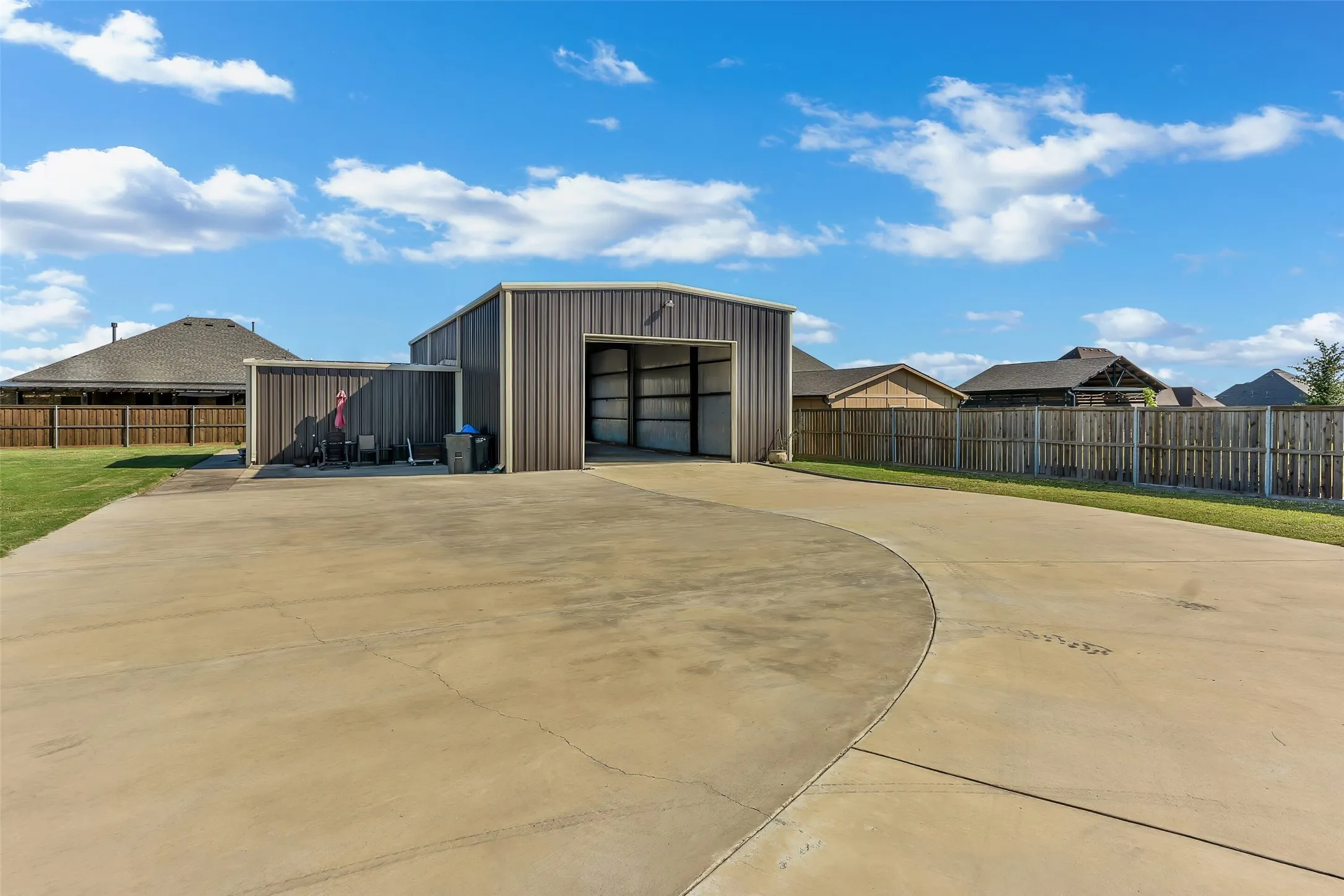 Metal workshop building featuring an open bay, an attached carport, and an expansive concrete driveway