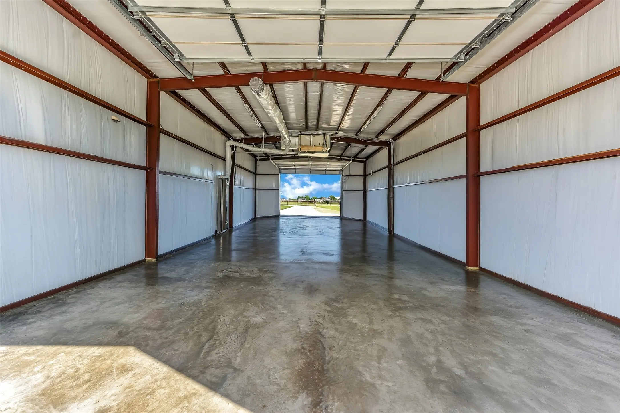 Spacious metal building featuring a concrete floor, exposed structural beams, white corrugated metal walls, and a high ceiling
