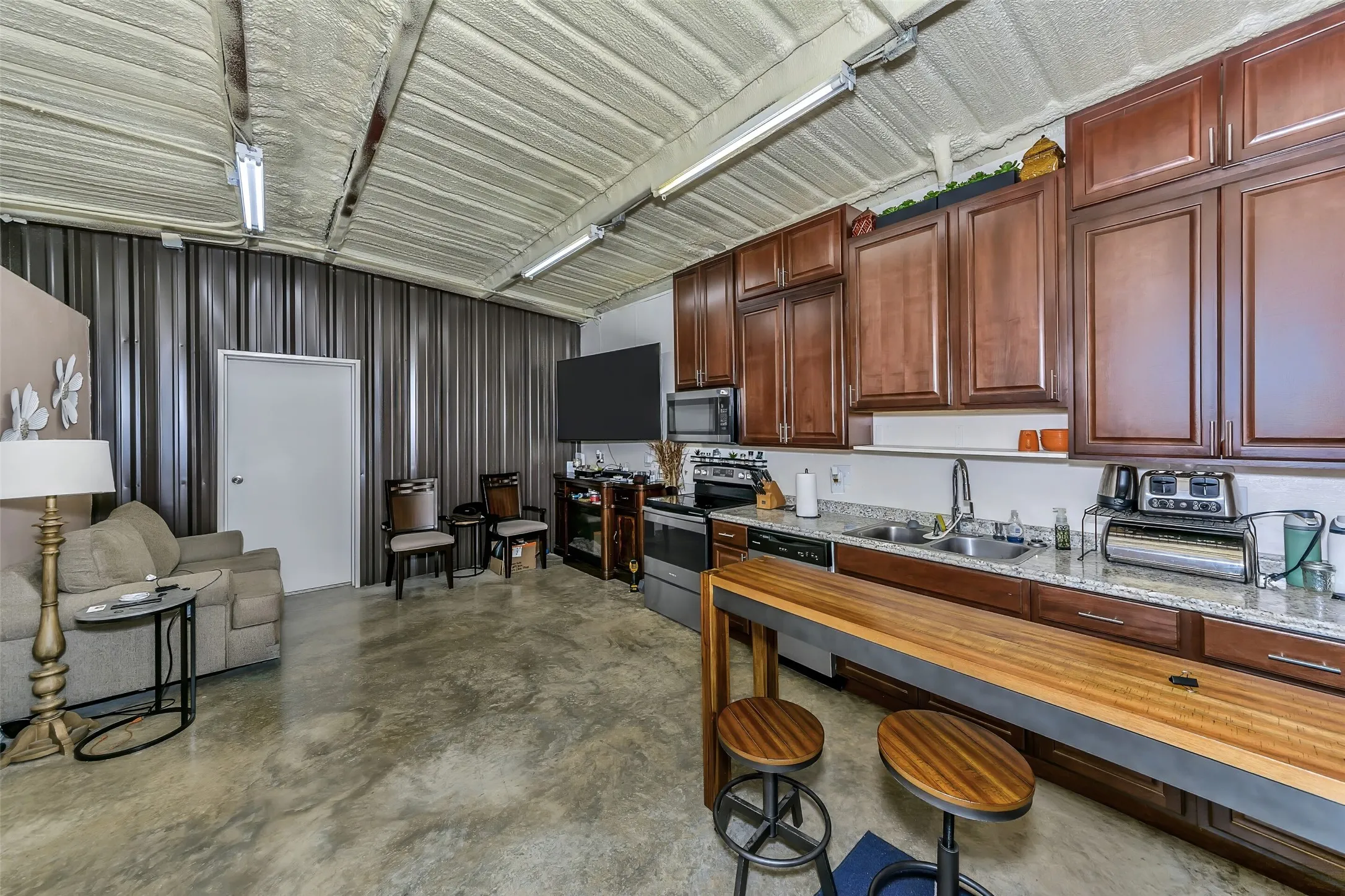 Open-concept living space featuring a full kitchen with wood-finish cabinetry, light-toned countertops, and stainless steel appliances