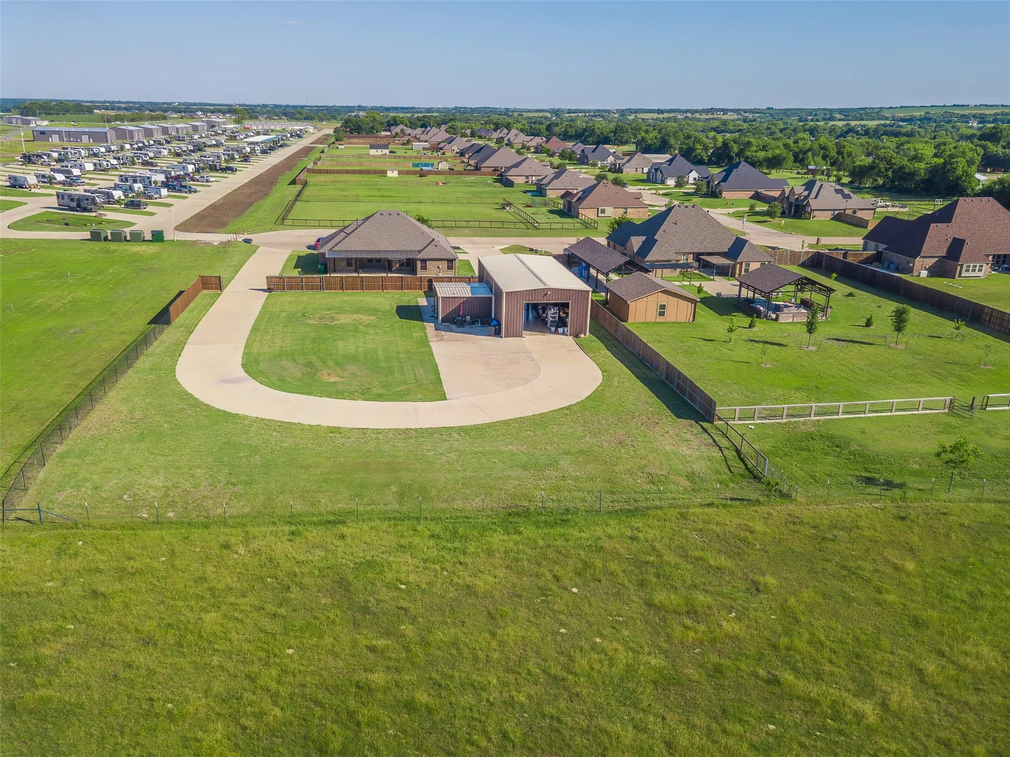 Expansive property featuring a large detached garage/workshop, a spacious concrete driveway, wood privacy fencing, and a covered outdoor patio structure