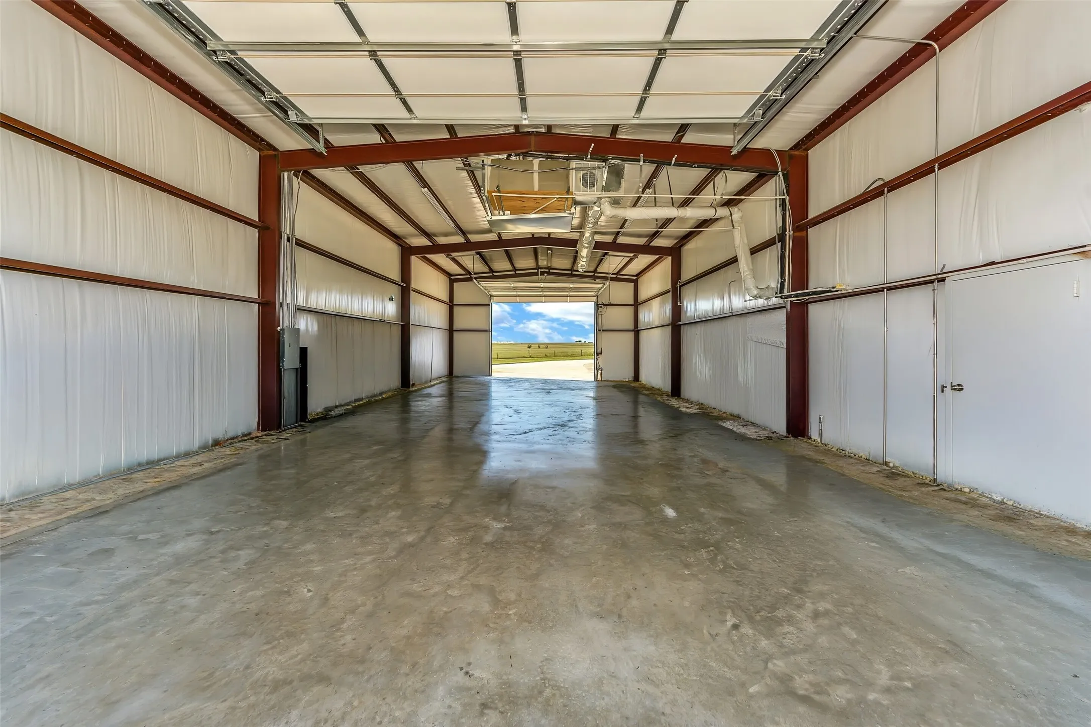 Spacious metal-frame interior featuring a concrete floor, white insulated panel walls, exposed structural beams, and a large overhead door