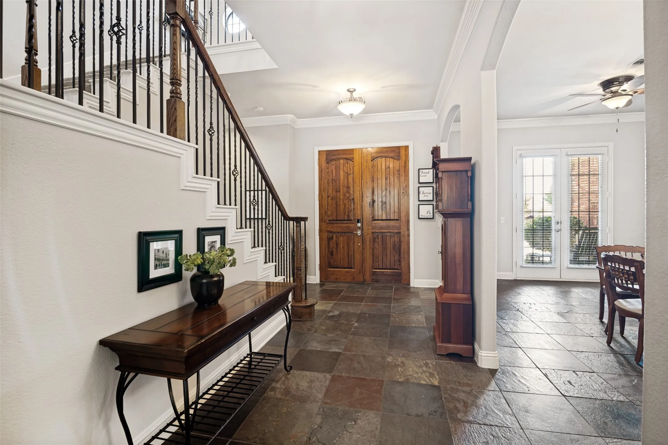 Entryway featuring slate tile flooring, wood double entry doors, a grand staircase with wrought iron balusters, and crown molding