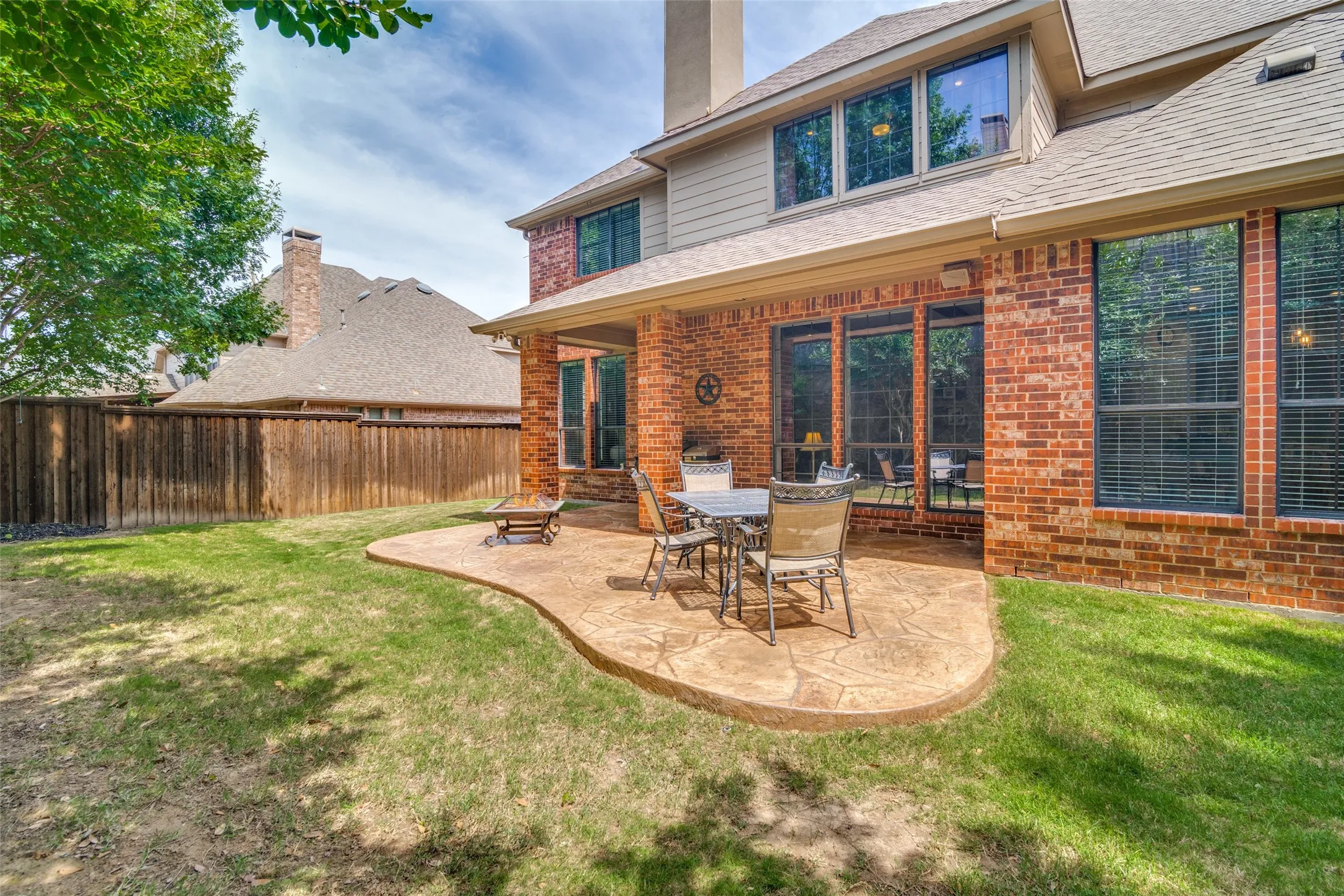 Expansive backyard featuring a stamped concrete patio, brick exterior, covered patio area, numerous large windows, and a privacy fence